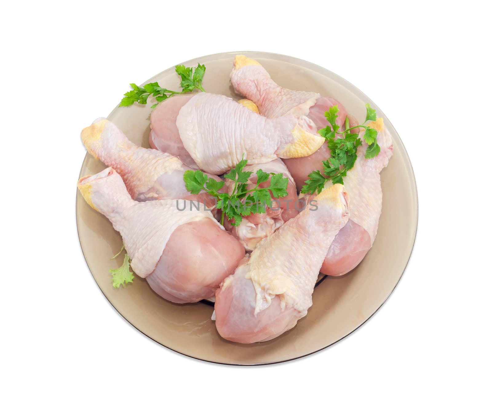 Top view of uncooked chicken legs and twigs of parsley on a glass dish on a light background
