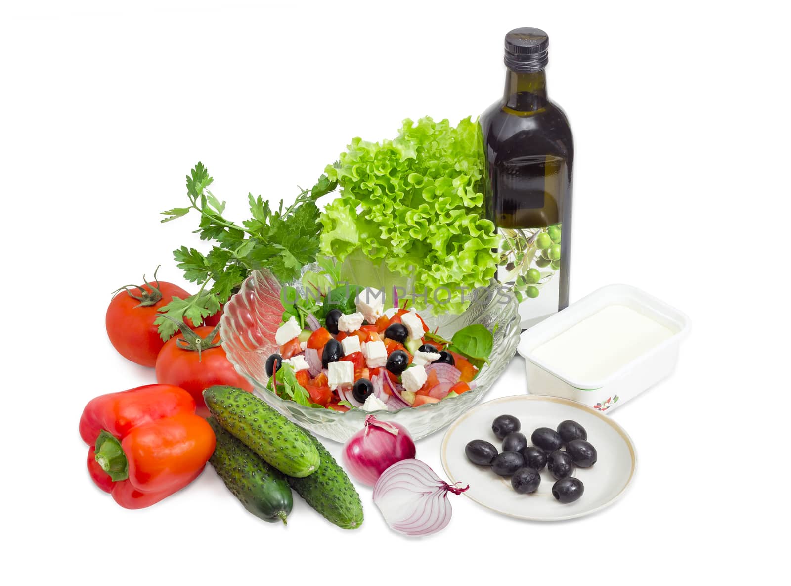 Greek salad in a glass salad bowl among ingredients for its cooking on a white background. 
