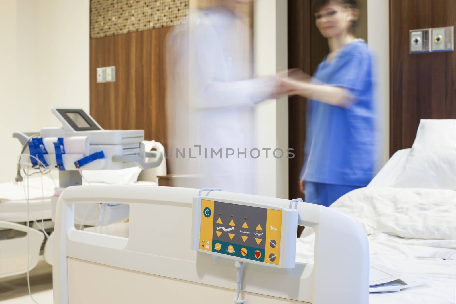 Blurred figures of doctor measuring the pulse of a patient in modern hospital room.