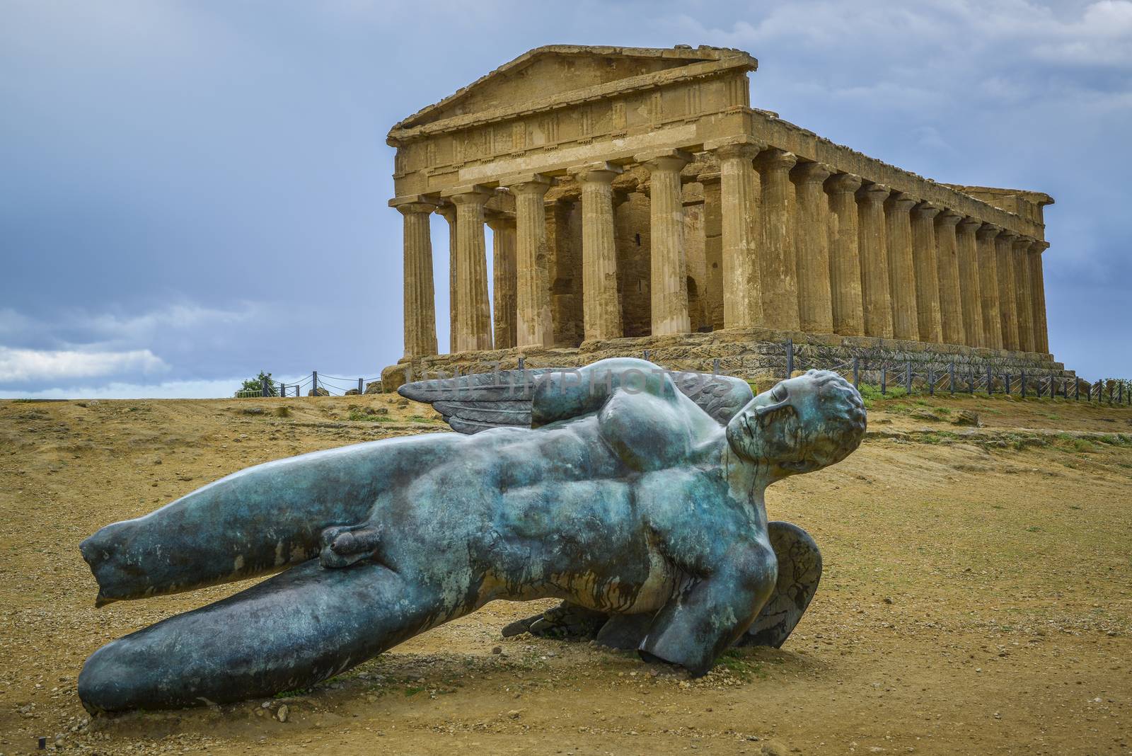 bronze statue of fallen ikaro on the background the concorde temple, Agrigento, Sicily, Italy