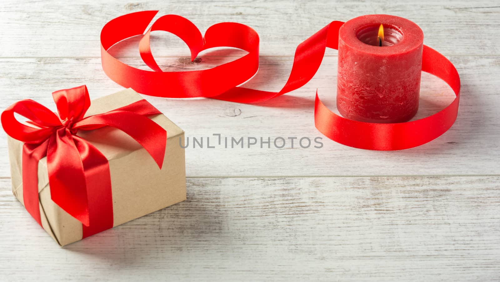 Box with a present to the Valentine's Day , red candle and tape on a white wooden table