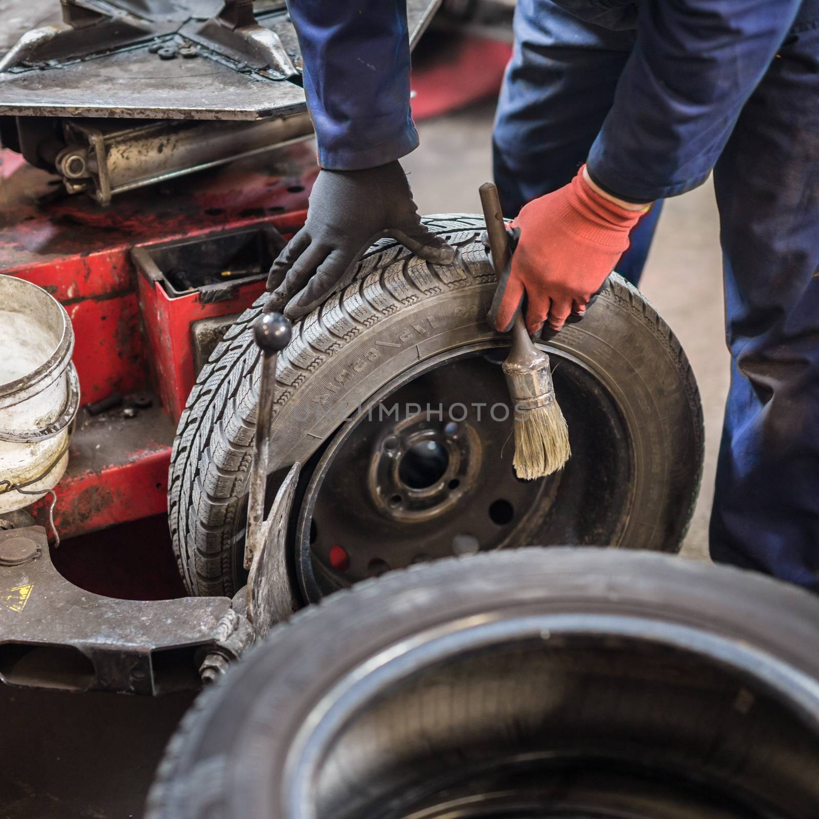 Professional auto mechanic replacing tire on wheel in car repair workshop.