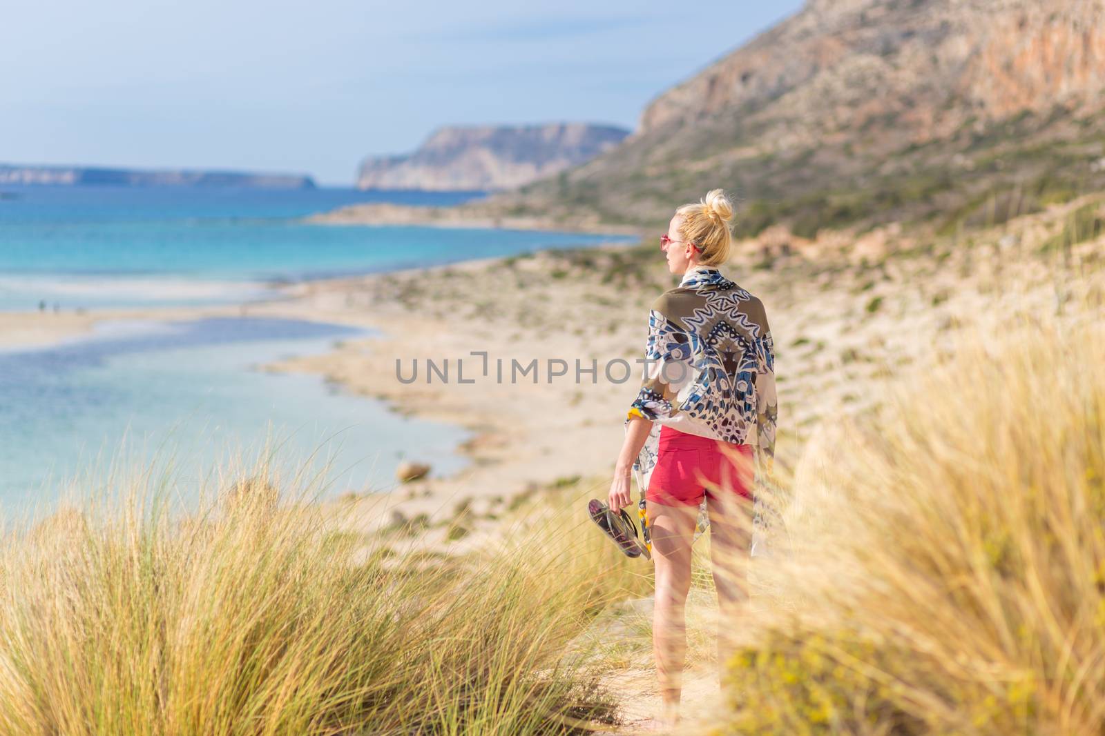 Relaxed woman wrapped in colorful scarf, enjoying sun, freedom and life at beautiful Balos beach in Greece. Concept of holidays, vacations, freedom, joy and well being.