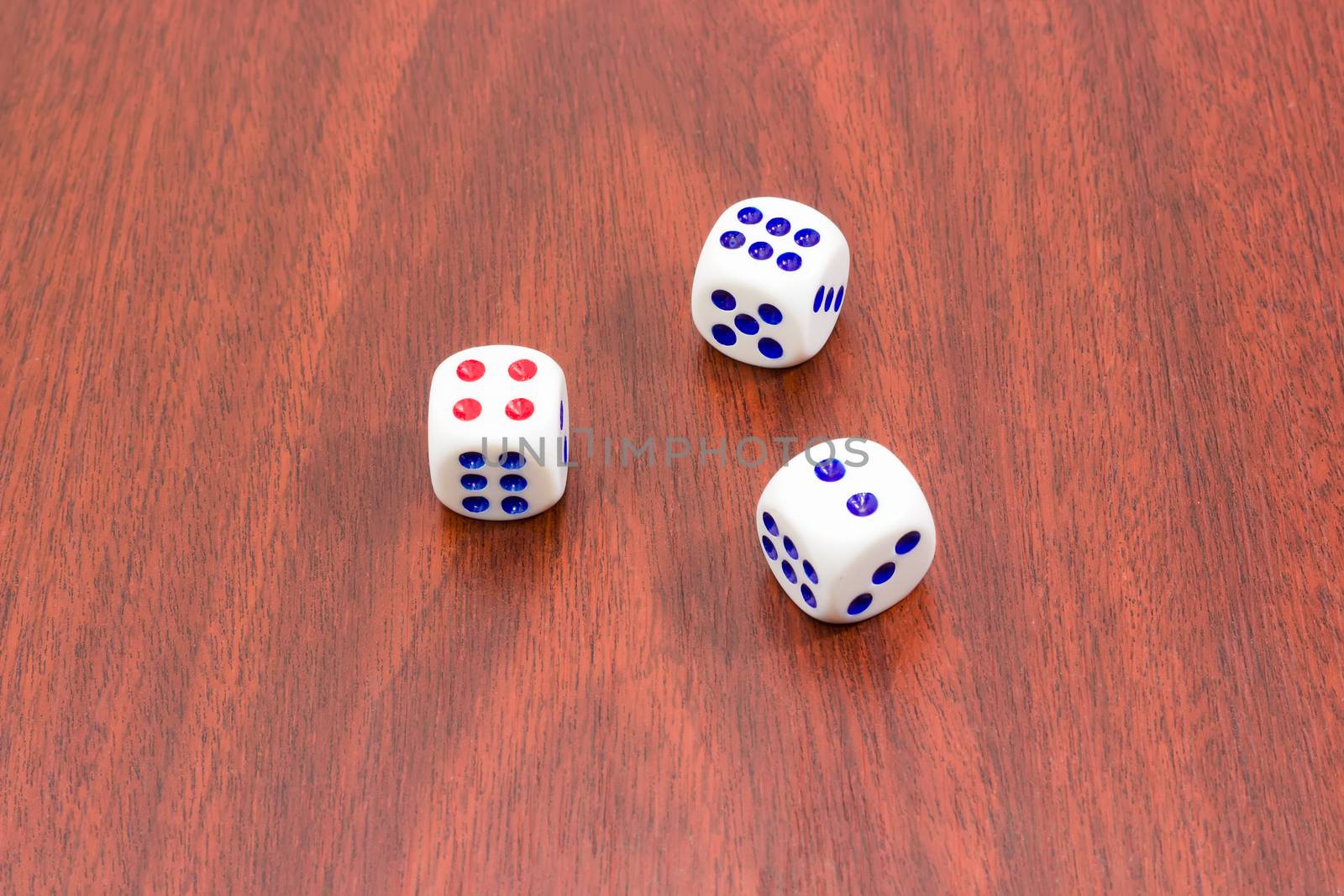 Three traditional plastic white six-sided dice with red and blue dots and rounded corners on wooden surface
