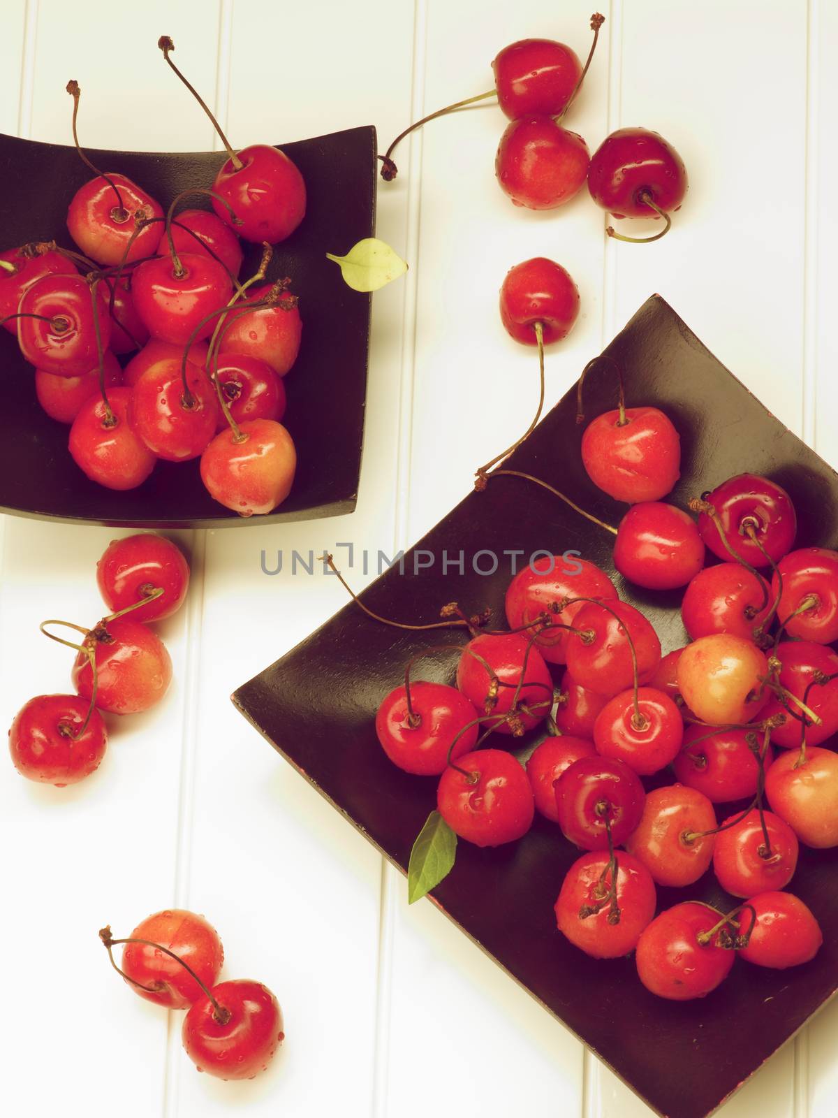 Arrangement of Two Black Plates with Fresh Ripe Sweet Maraschino Cherries closeup on Plank White background. Retro Styled