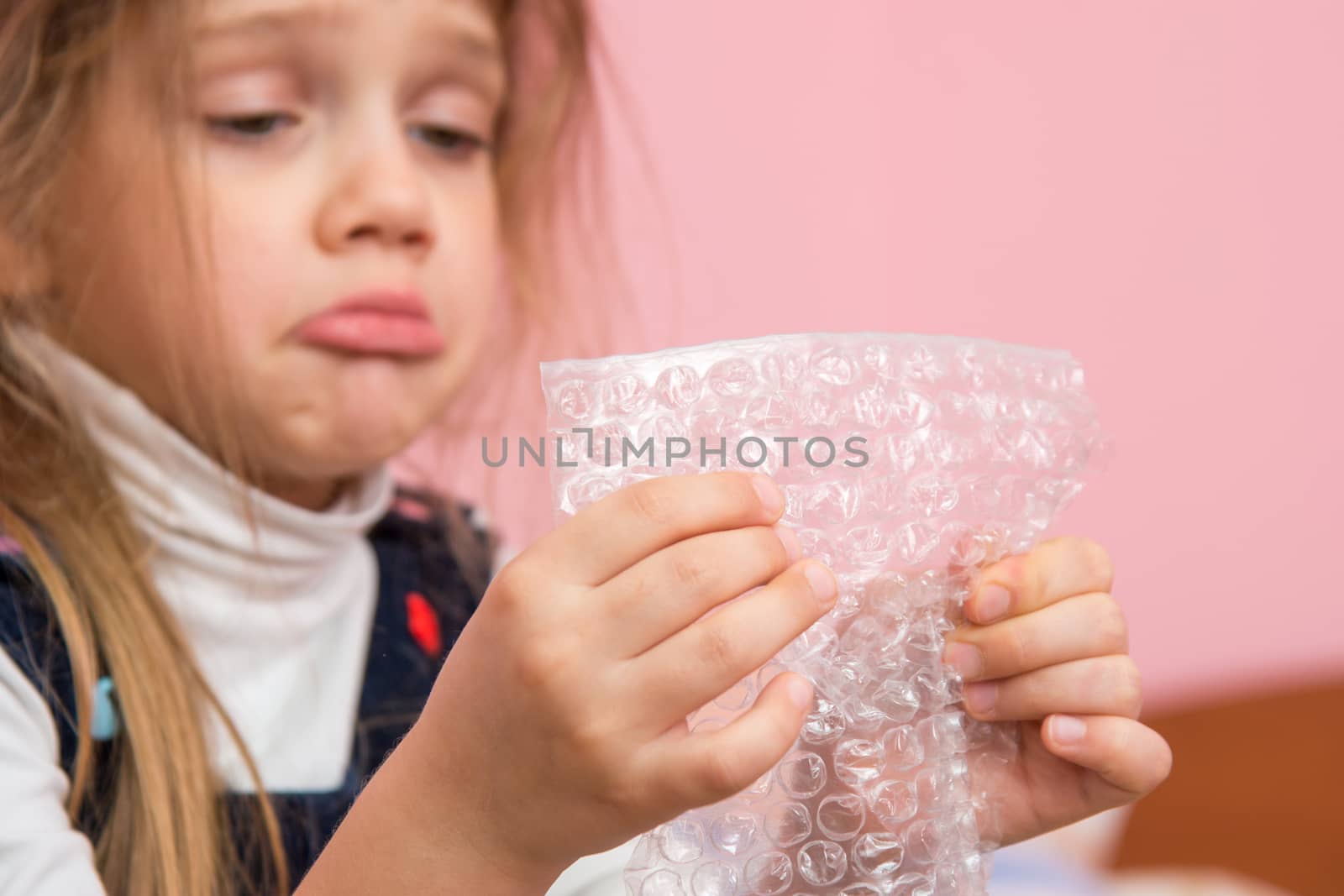 Upset girl pouting cheeks eats bubbles packaging film