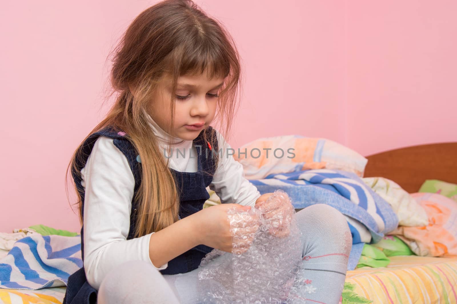 Sad girl sitting on the bed and eats bubbles on the packaging film