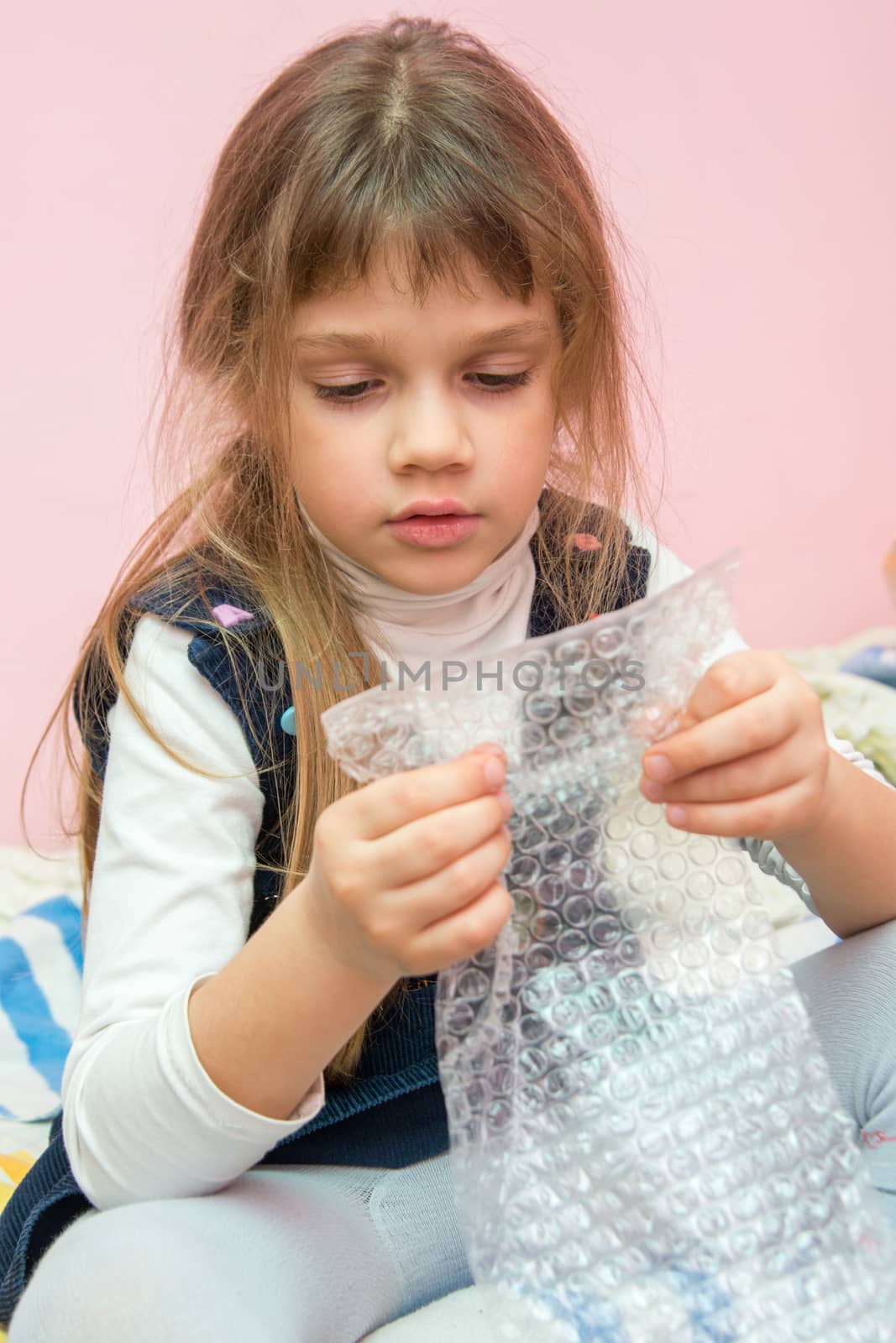 Five-year girl sitting on the bed and eats bubbles packaging package