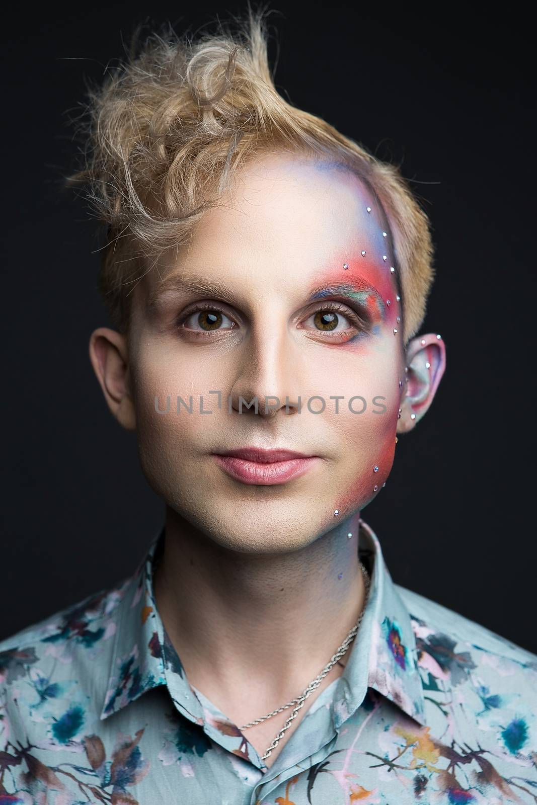 Portrait of beautiful young man with modern hairstyle, artistic multicolor makeup and rhinestones on the face. Studio shot. Black background