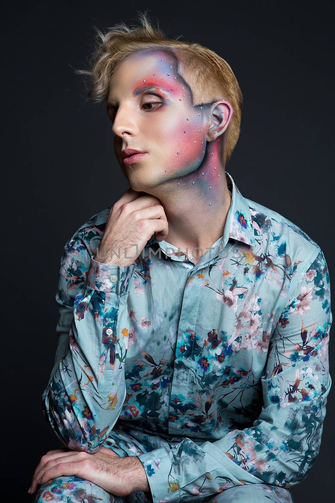 Portrait of beautiful young man with modern hairstyle, artistic multicolor makeup and rhinestones on the face. Studio shot. Black background