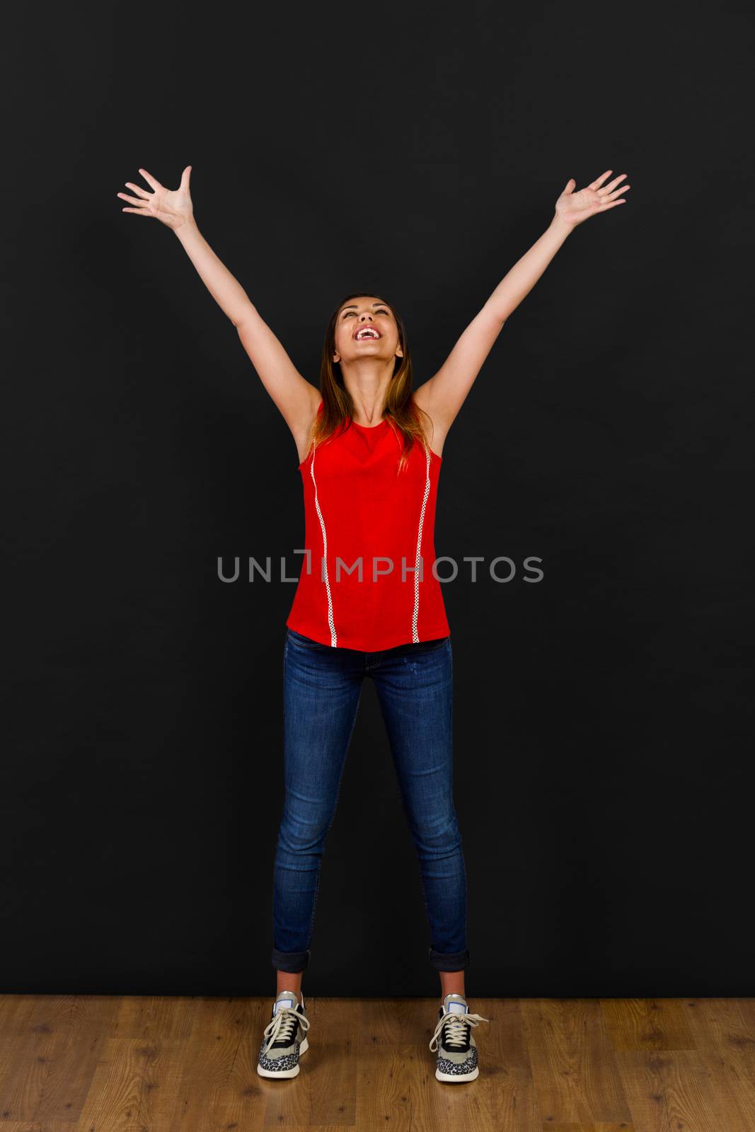 Beautiful happy woman with arms open in front of a black wall