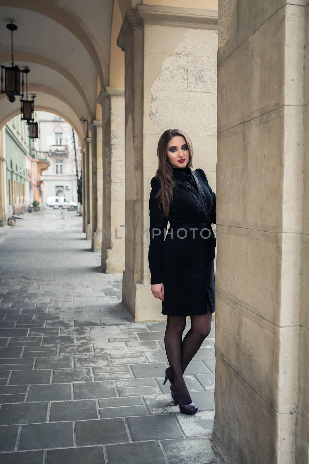 beautiful girl stands under the arch in the city