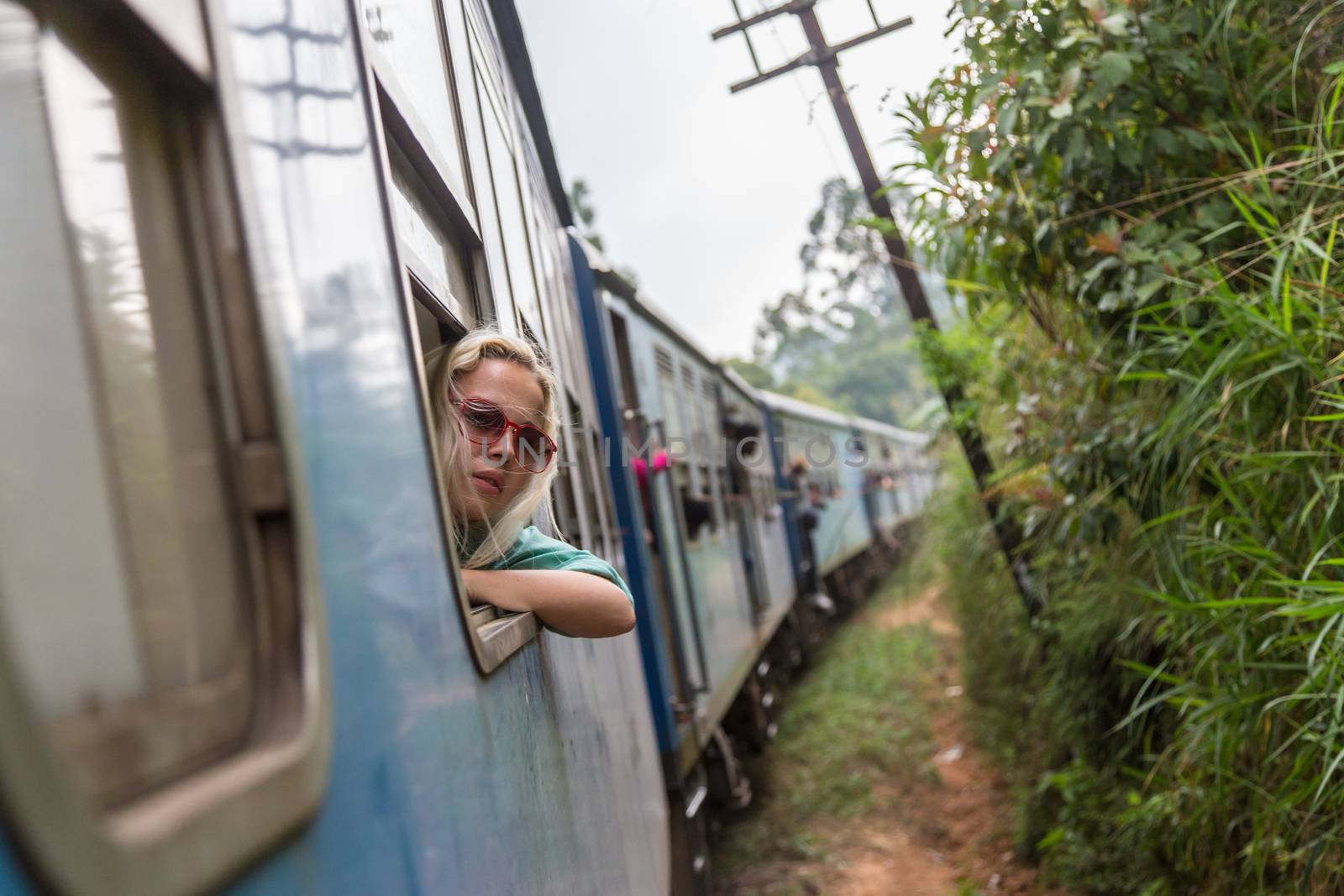 Blonde caucasian woman looking trough old retro blue train window , traveling by train in third world country.