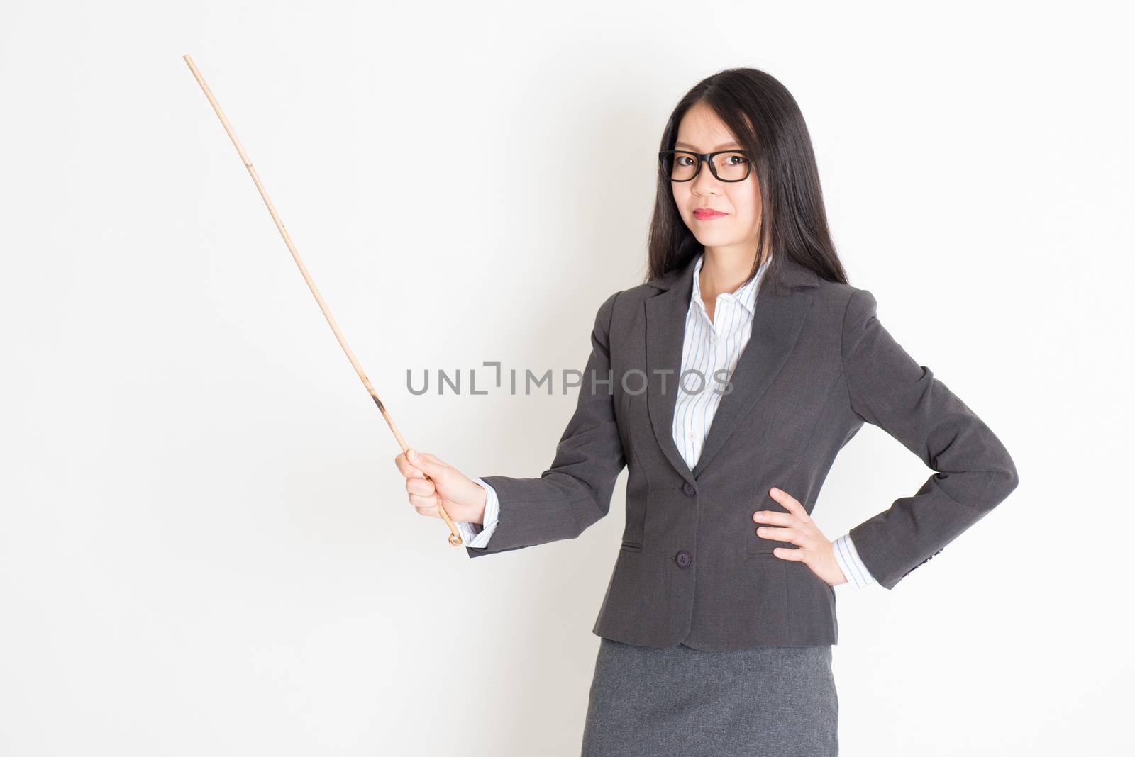 Asian female teacher hand holding a cane in class lesson, standing on plain background.