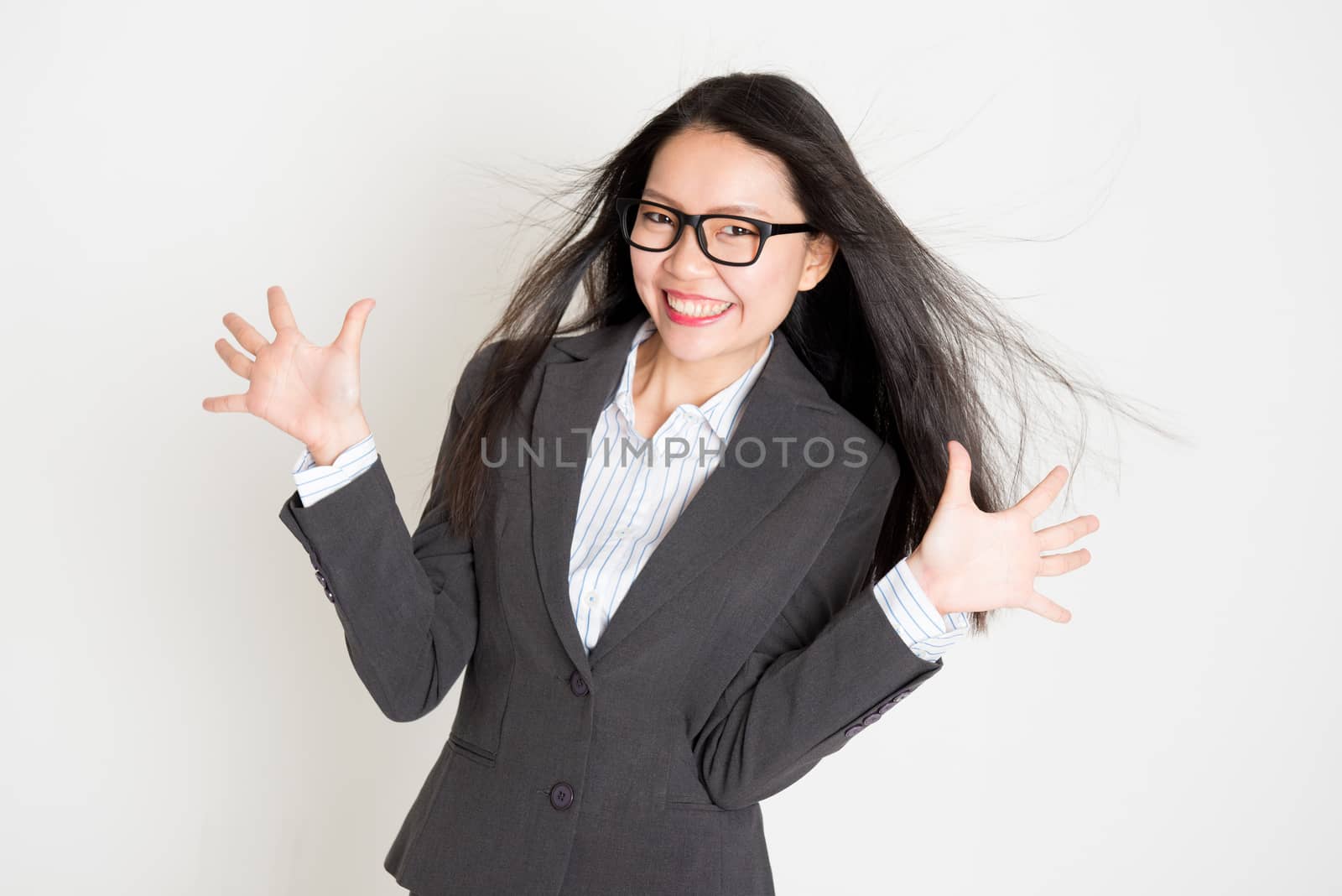 Portrait of happy Asian businesswoman in formalwear smiling and palms open, standing on plain background.