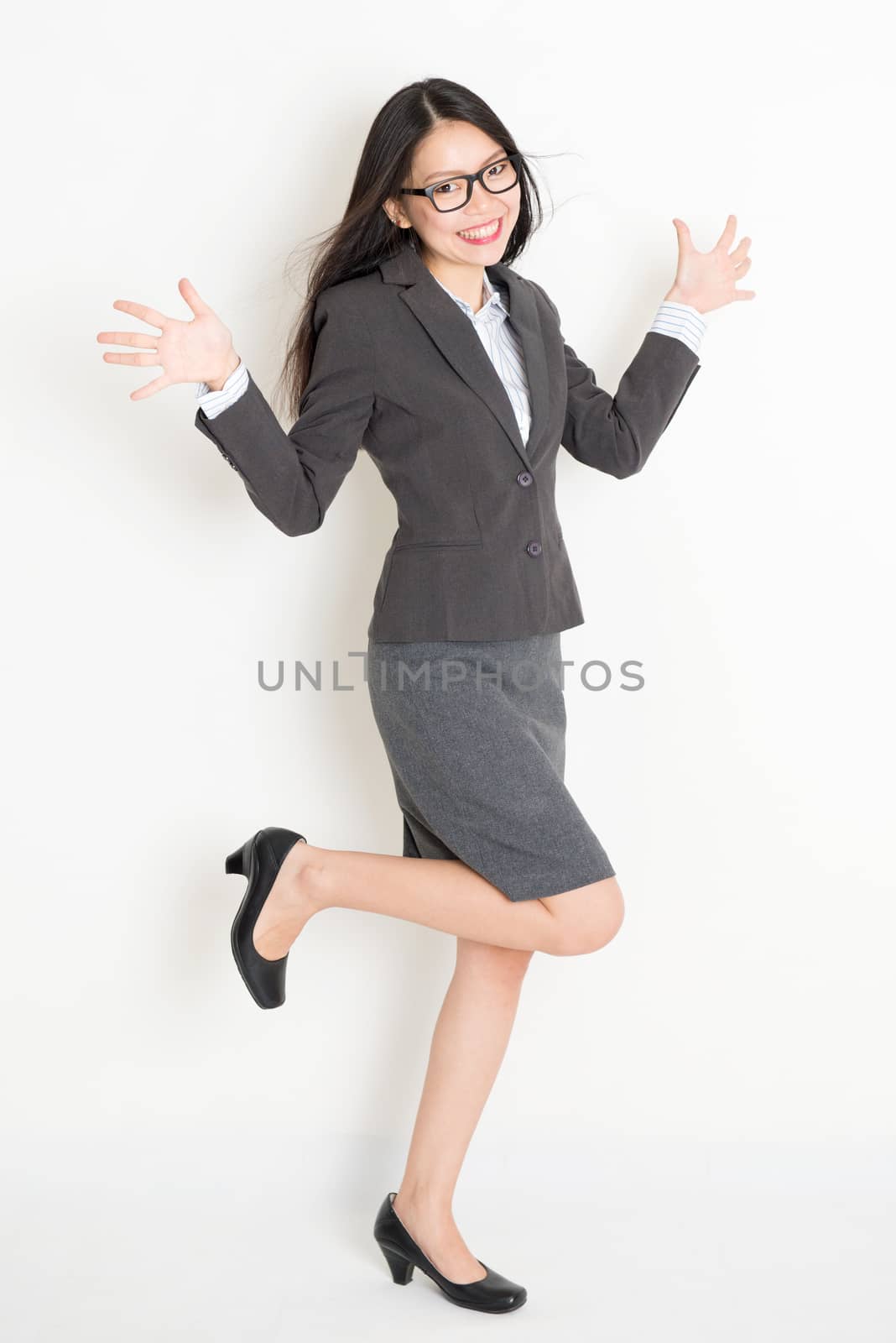 Portrait of happy Asian businesswoman in formalwear smiling, full body standing on plain background.