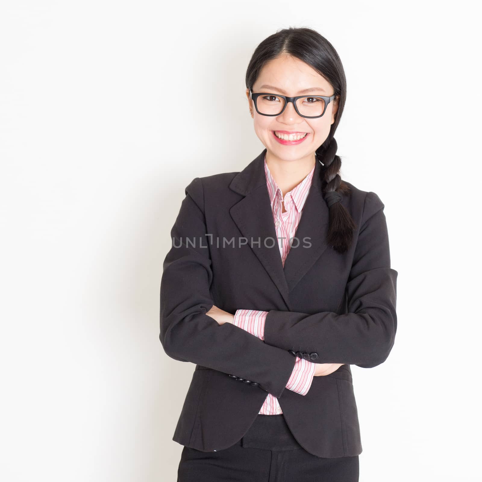 Portrait of Asian businesswoman in formalwear smiling and looking at camera, standing on plain background.
