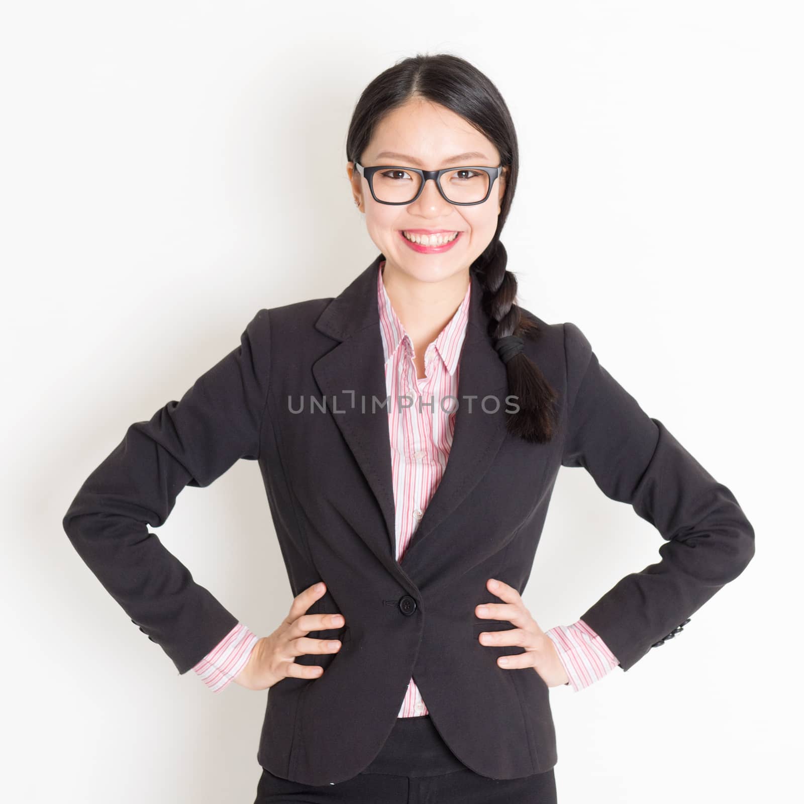 Portrait of Asian business woman in formalwear smiling and looking at camera, standing on plain background.