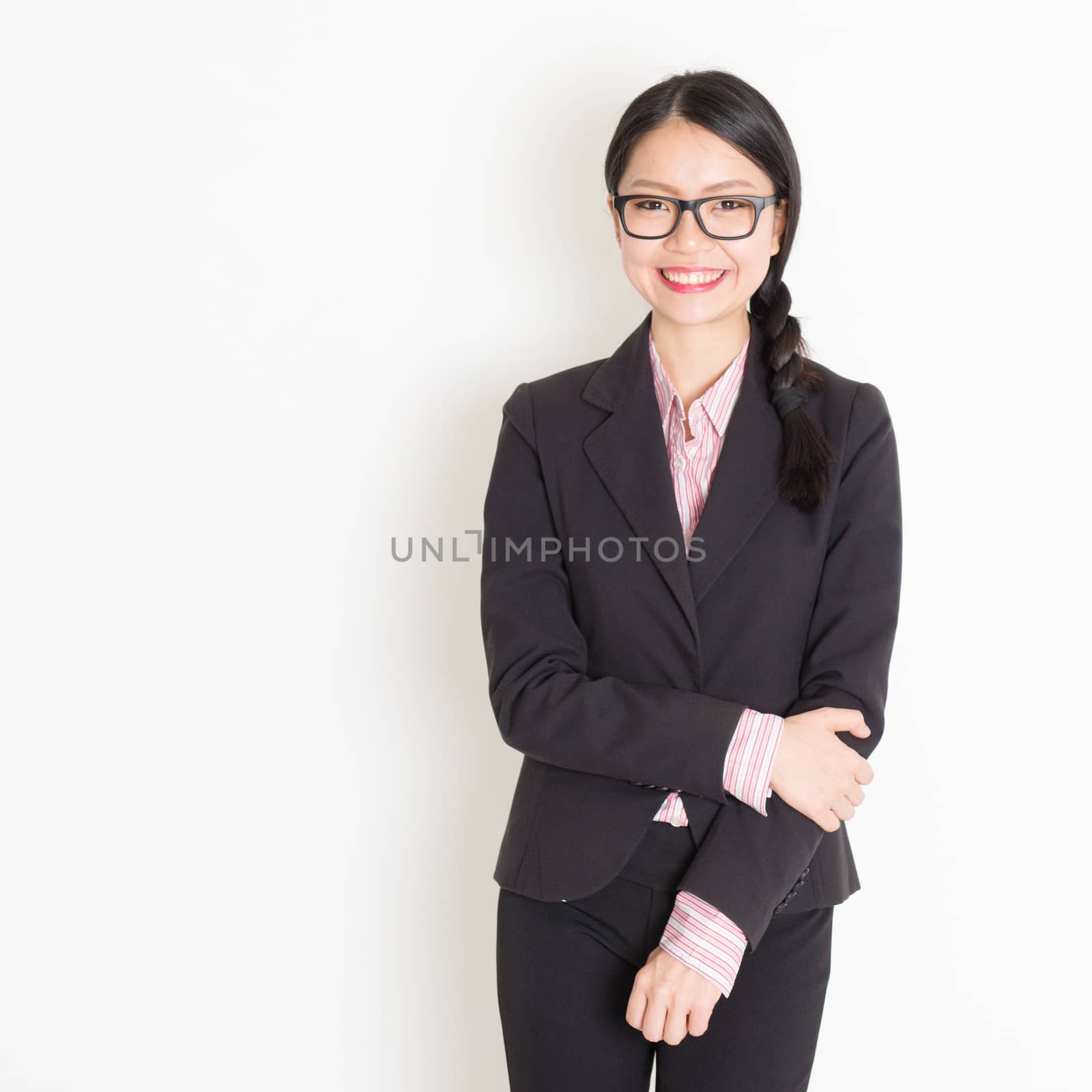 Asian businesswoman in formalwear smiling and looking at camera, standing on plain background.