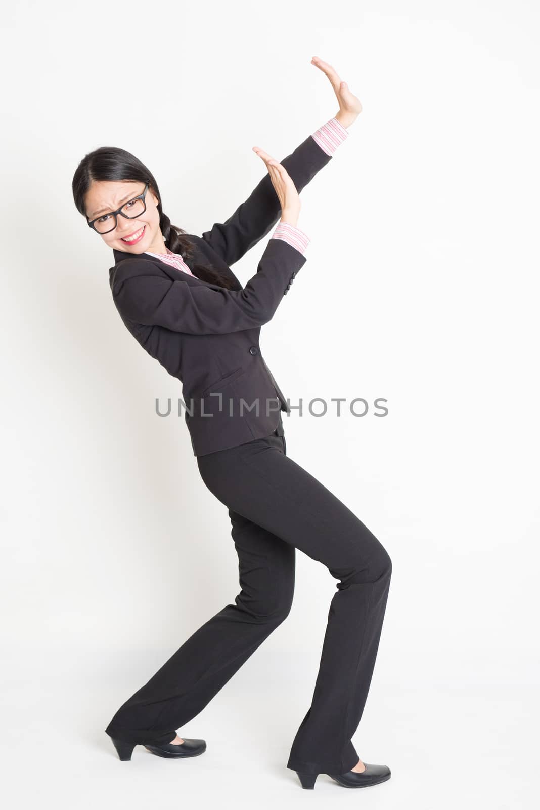 Full body portrait of young Asian businesswoman in formalwear hands defending on something, standing on plain background.