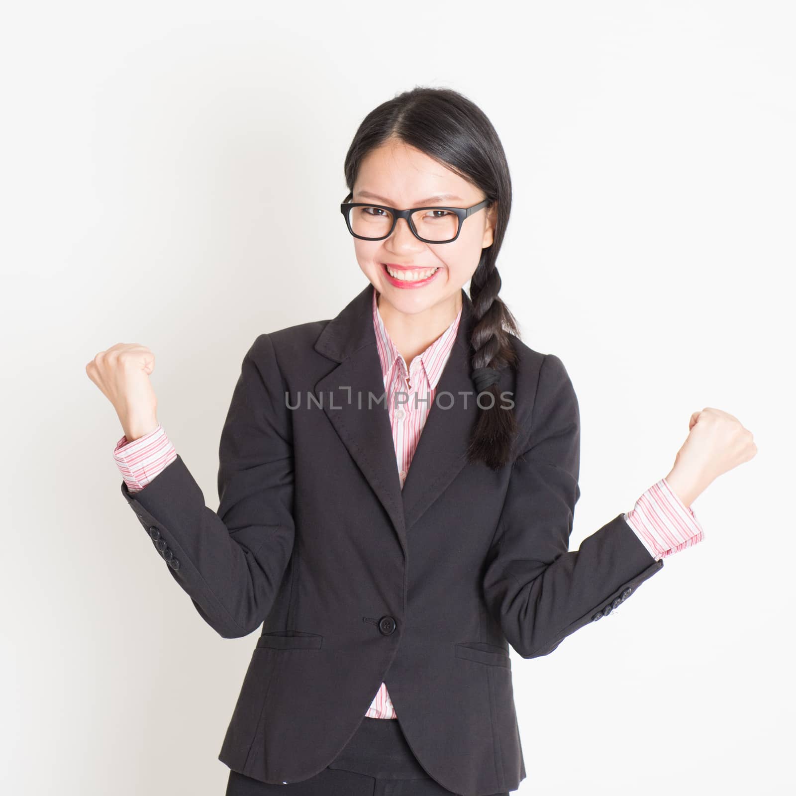 Portrait of Asian businesswoman in formalwear smiling and celebrating success, standing on plain background.