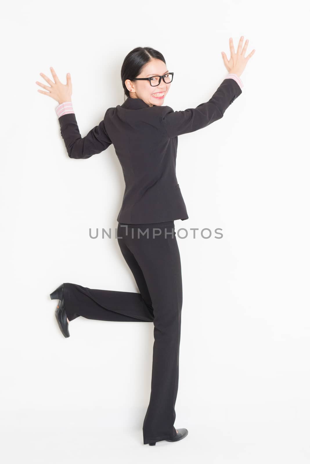 Businesswoman in formalwear hands pushing against wall, full body standing on plain background, copy space.