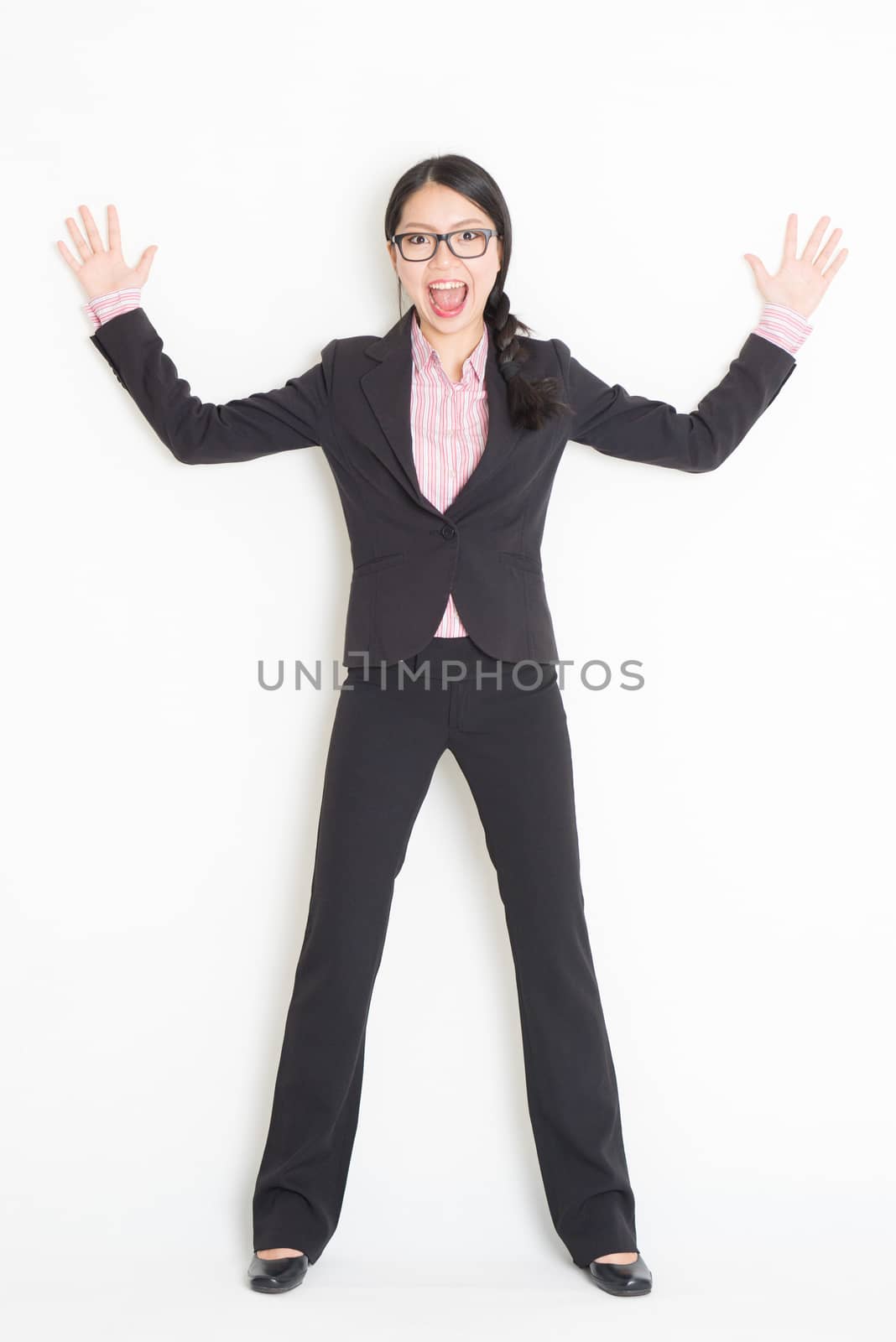 Full length front view of shocked young Asian businesswoman in formalwear leaning on wall, standing on plain background.