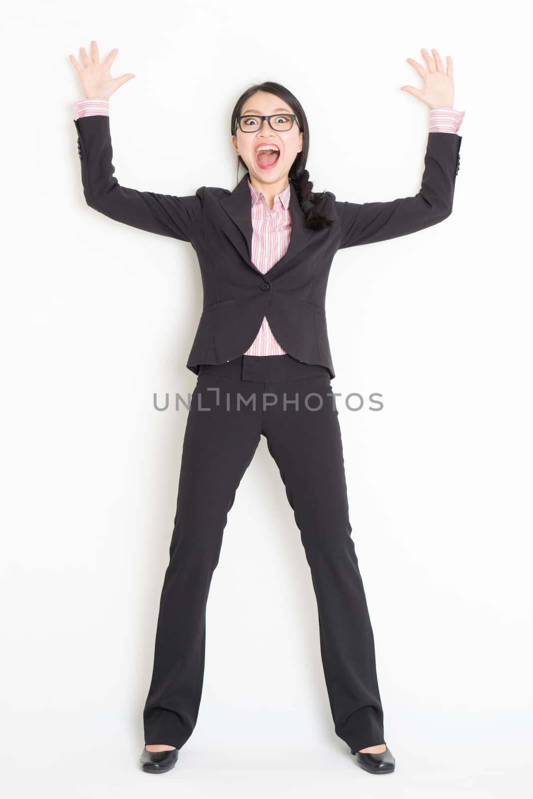 Full length front view of shocked young Asian businesswoman in formalwear bang and leaning on wall, standing on plain background.