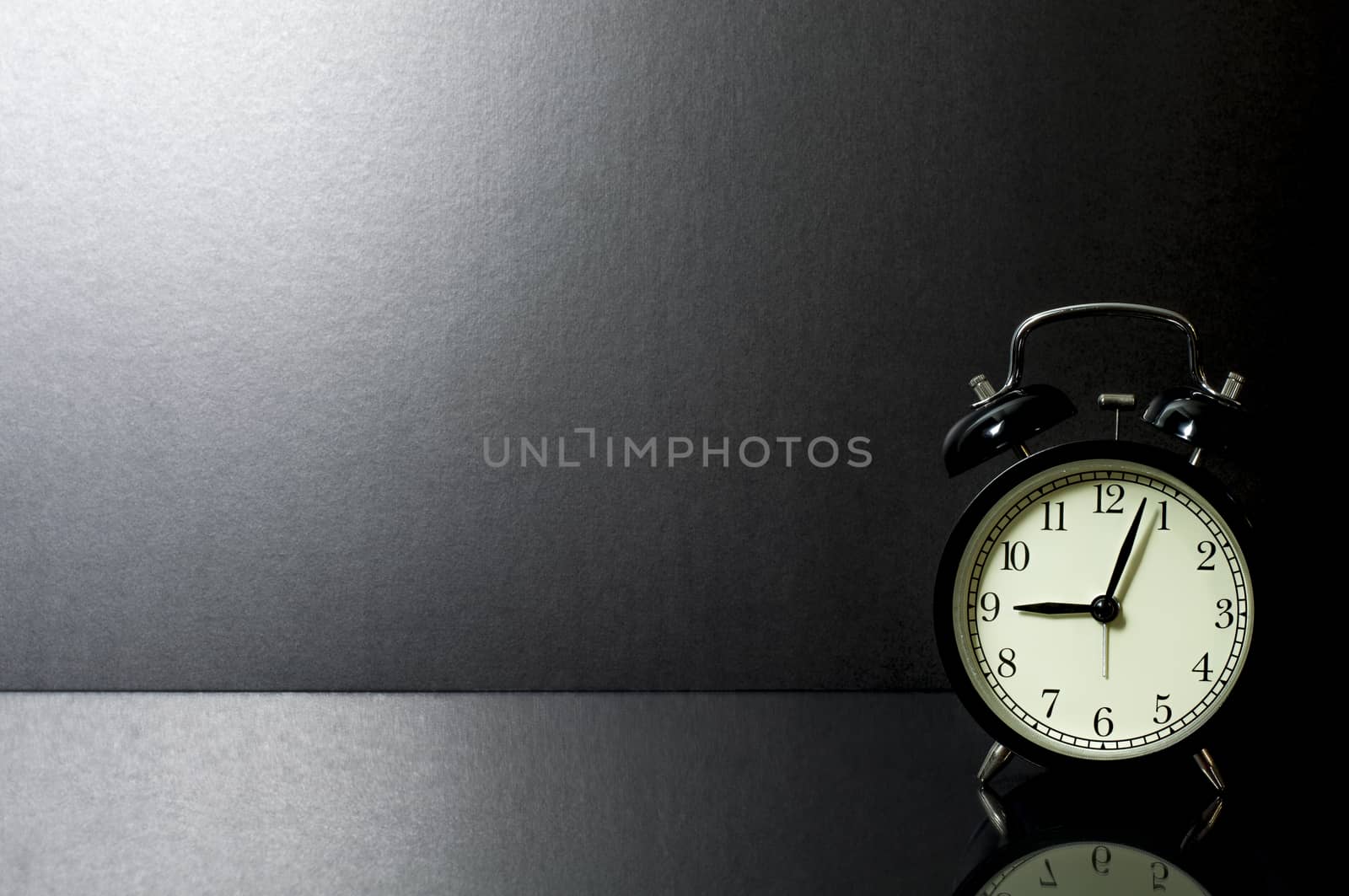 Still Life retro alarm clock on glass table in front of black background.