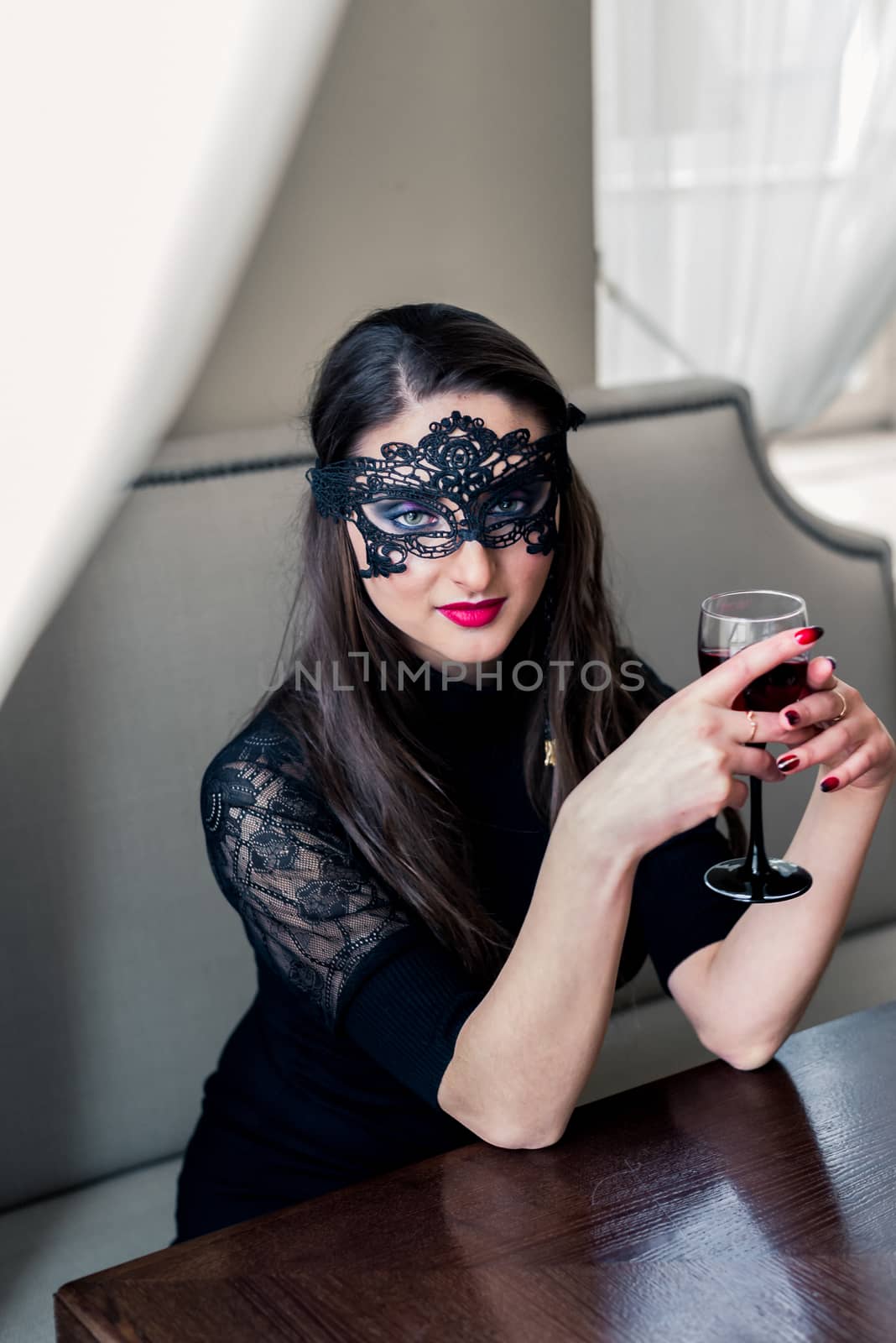 a beautiful girl sitting in the cafe with black mask and wine