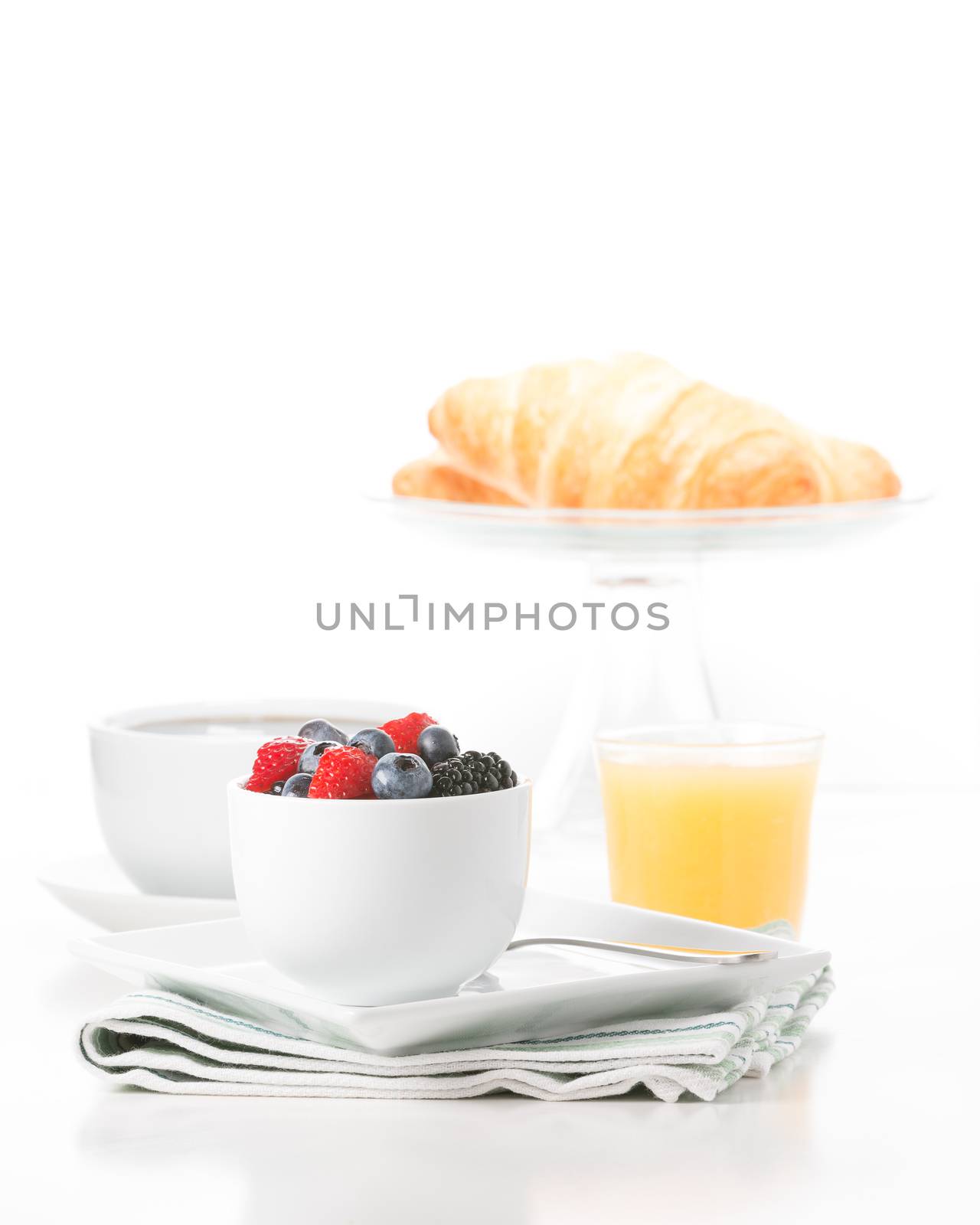 Small bowl of fresh berries served with croissant, coffee and orange juice.