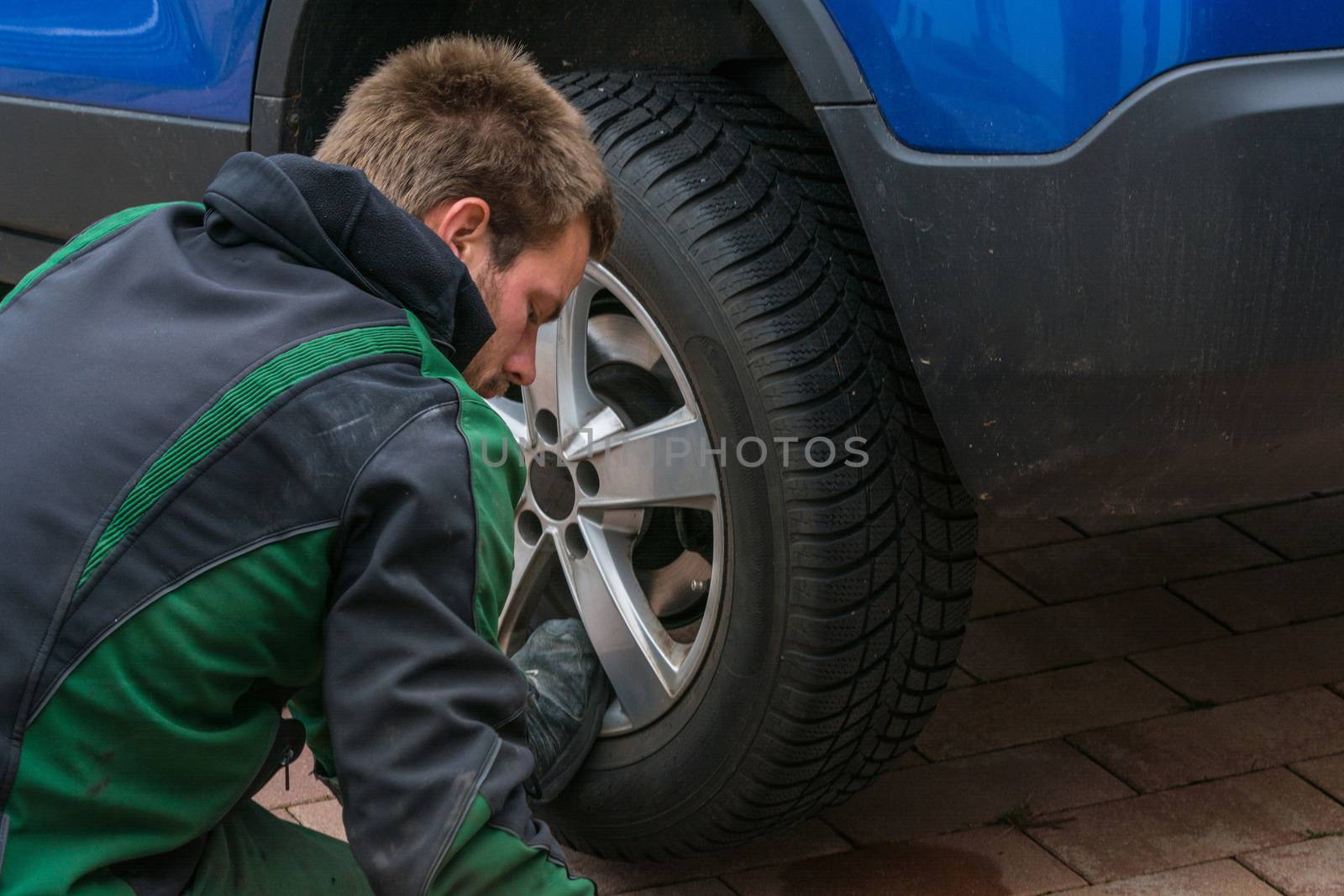 Young man  exchanging the car tires. From summer tires on winter tires on his car.