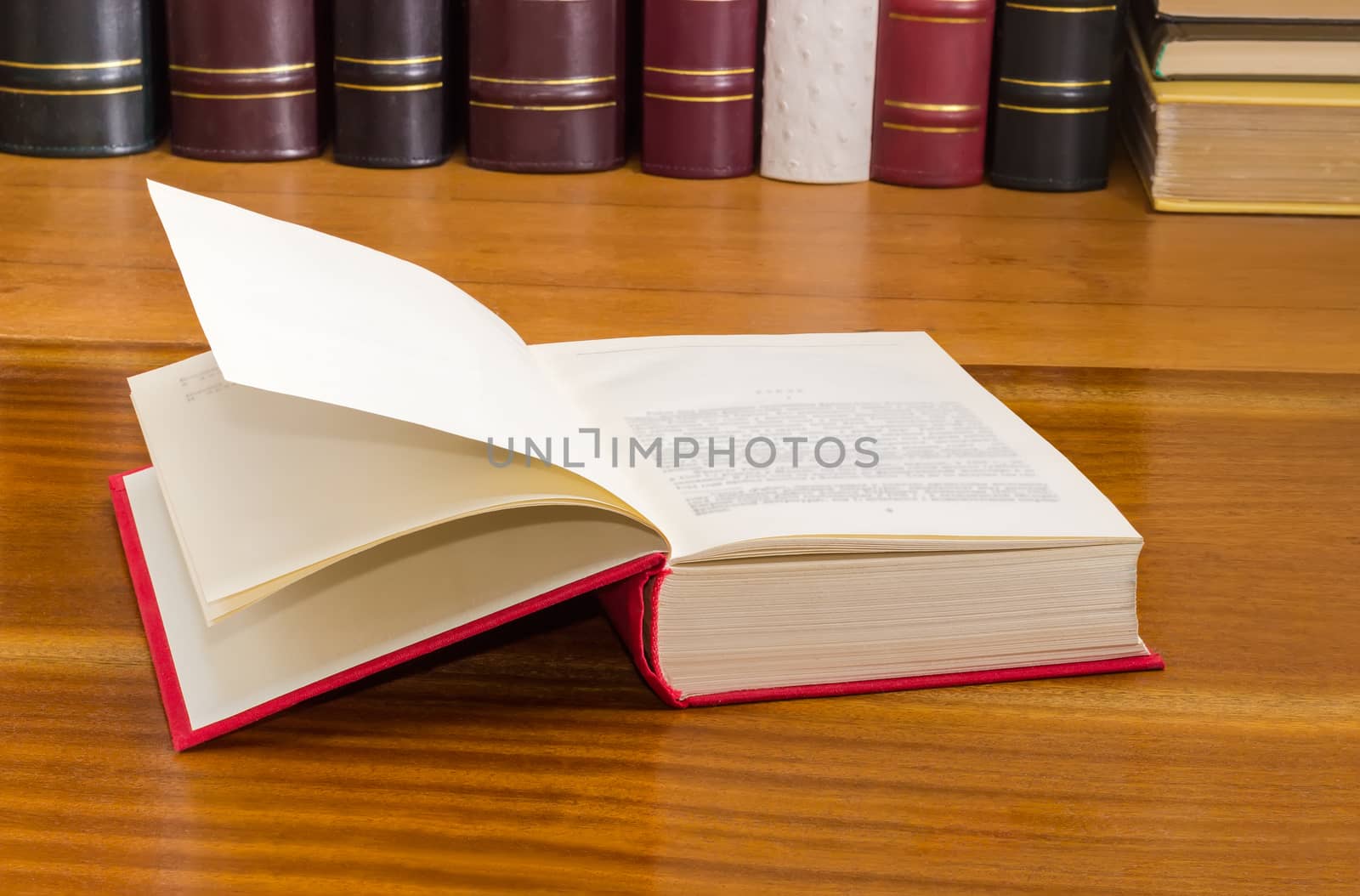 Open book with red cover on a wooden table against of the other books on the background
