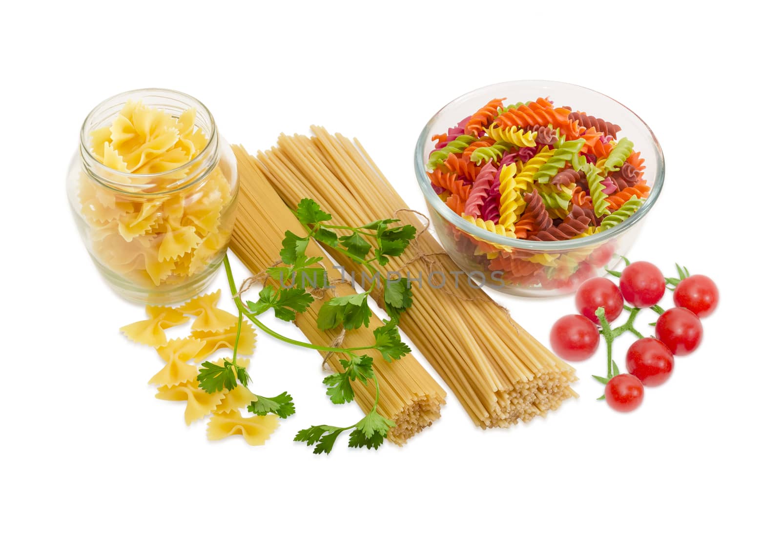 Uncooked dried long pasta two varieties, colored spiral pasta and farfalle pasta, sprigs of parsley and cluster of cherry tomatoes on a light background
