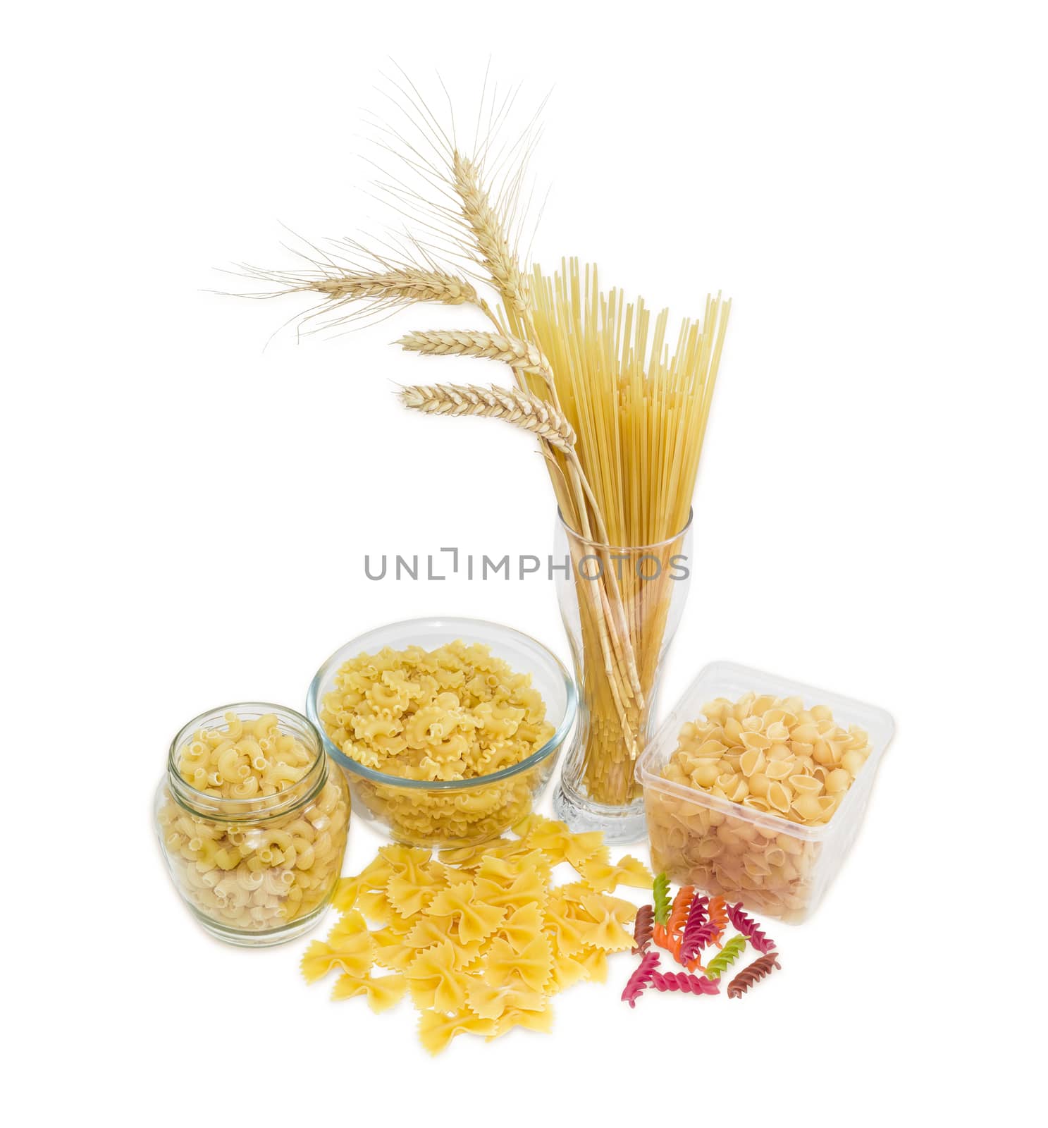 Uncooked dried long pasta and wheat spikes in glass, other pasta different varieties, shapes and colors on a light background
