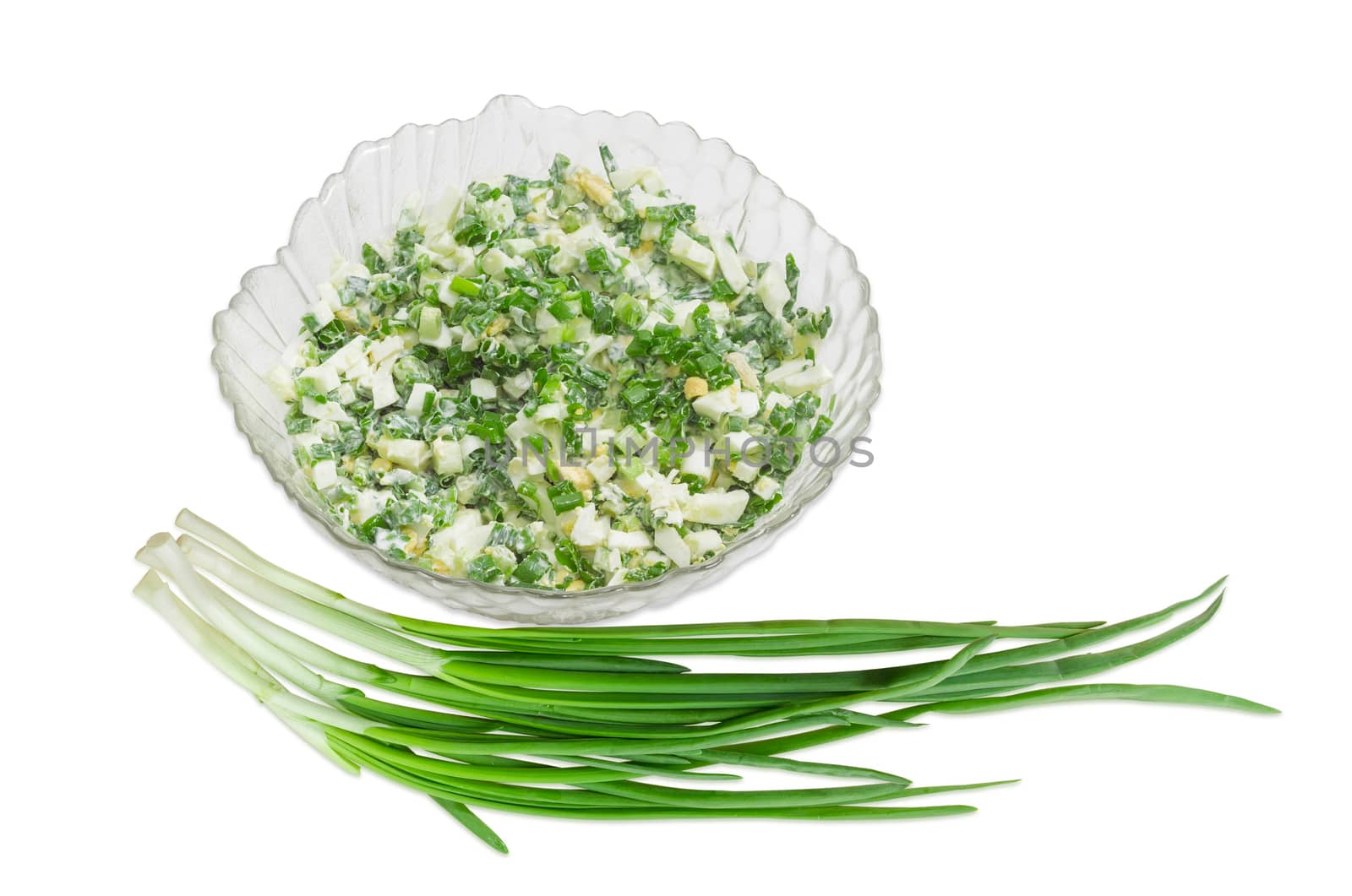 Spring salad with chopped green onions, boiled eggs and sour cream in a glass salad bowl and a bunch of green onions on a light background
