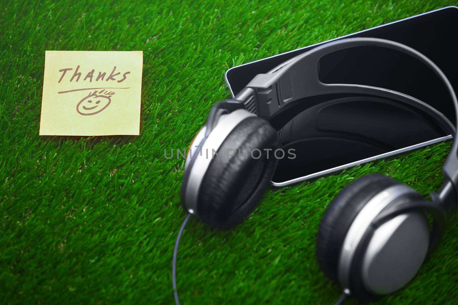 Thanks text on sticky note on a grass with headphones and digital tablet
