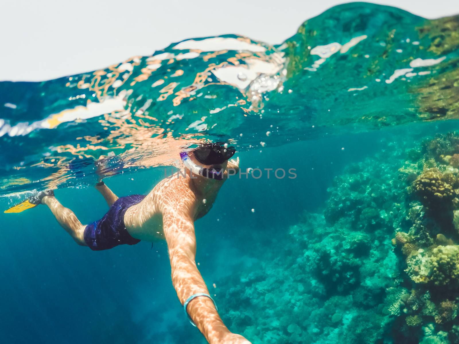 Underwater and surface split view in the tropics paradise with snorkeling man, fish and coral reef, under and above waterline, beautiful view on tropical sea. Egypt. Holiday snorkeling vacation concept