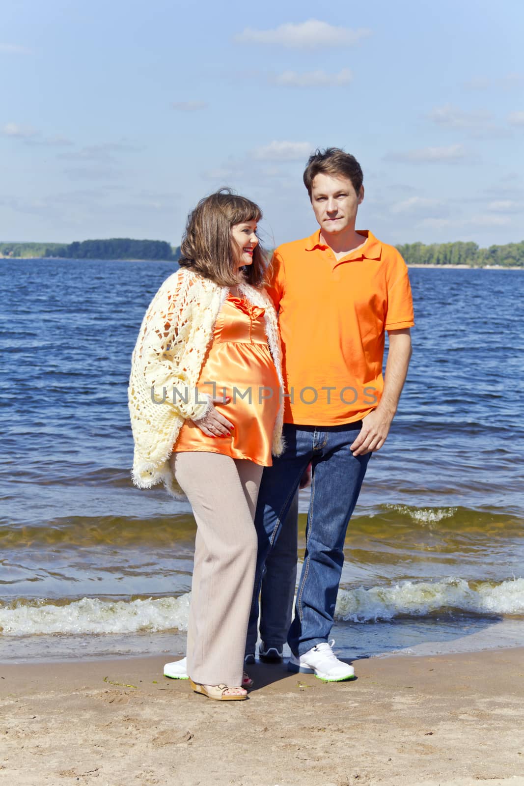 Husband embraces pregnant wife near river