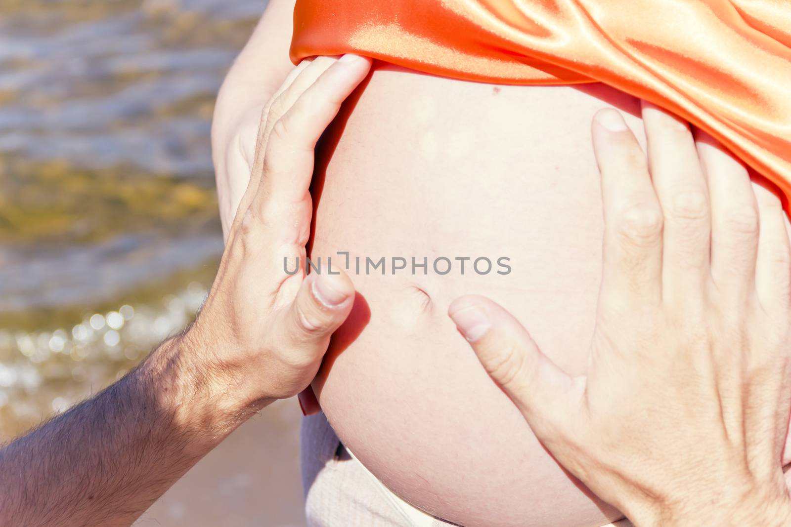 Husband hands embraces stomach of his pregnant wife in summer time