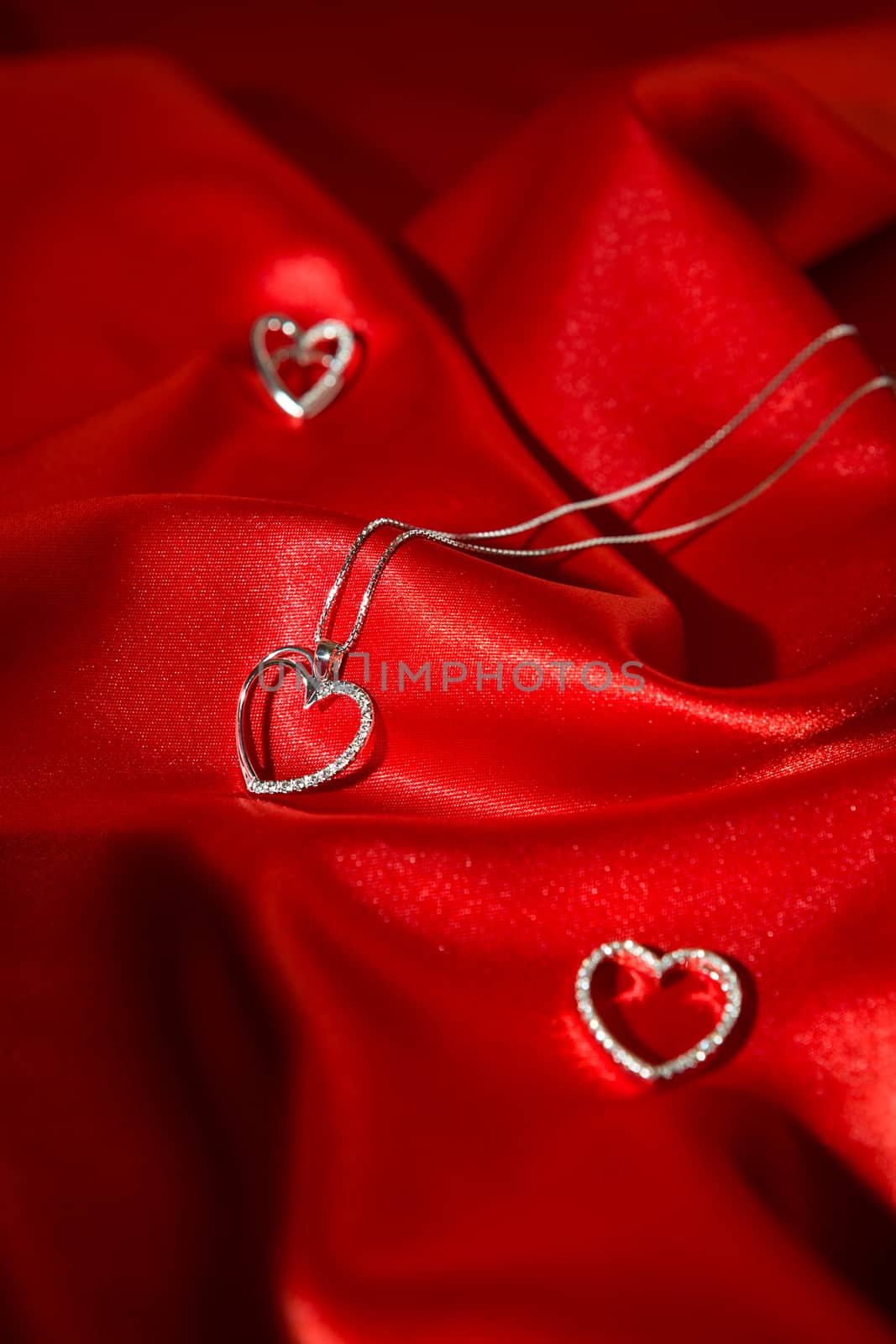 Silver heart pendants over a red satin background