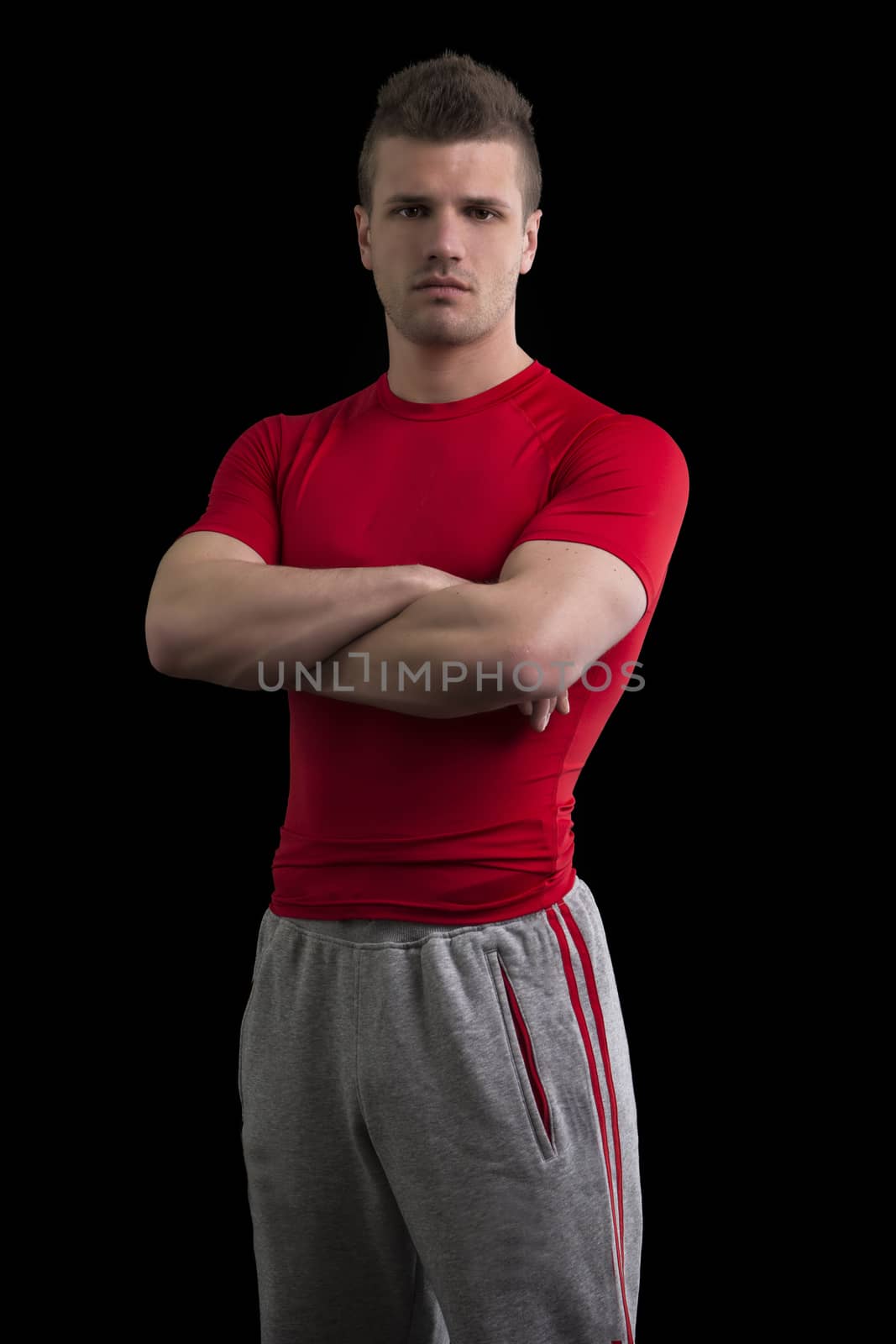 Handsome young personal trainer in studio, isolated on black background, with arms crossed on his chest