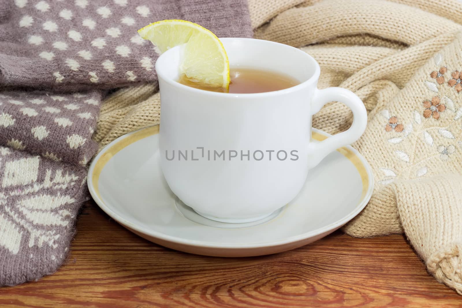 White cup of black tea with lemon on a background of women's woolen mittens and knitted scarf closeup on a wooden surface
