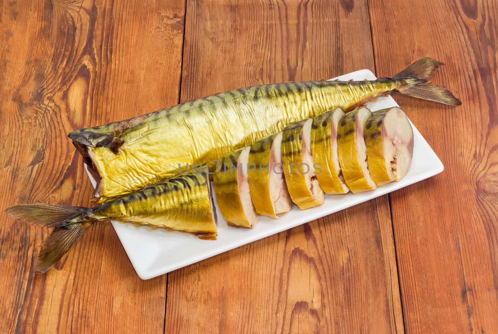 One sliced and one whole cold-smoked Atlantic mackerel on a rectangular white dish on an old wooden surface
