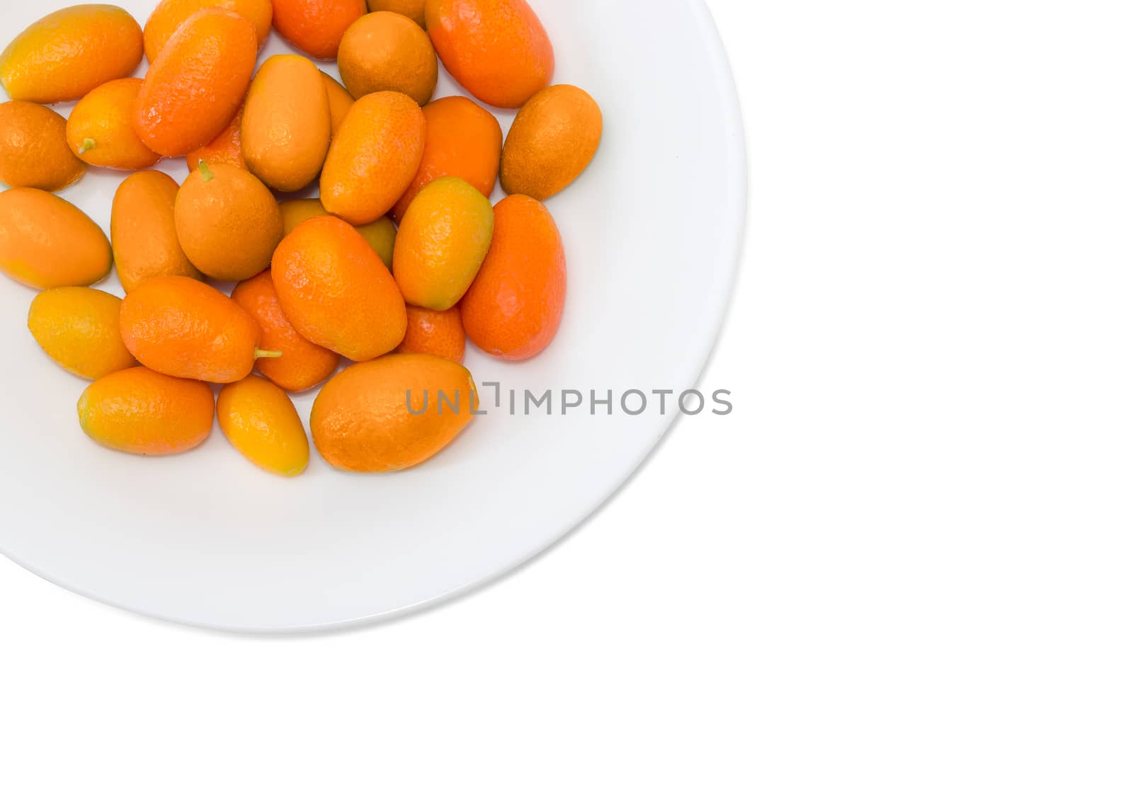 Top view of fragment of white dish with fresh oval kumquats closeup on a light background
