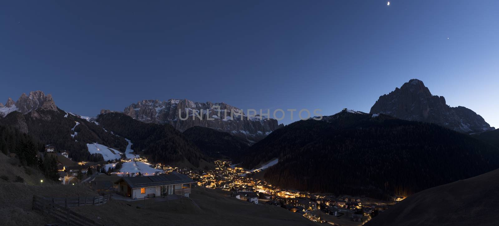 blue hour in Selva di Val Gardena with the moon above the Sassolungo Group profile