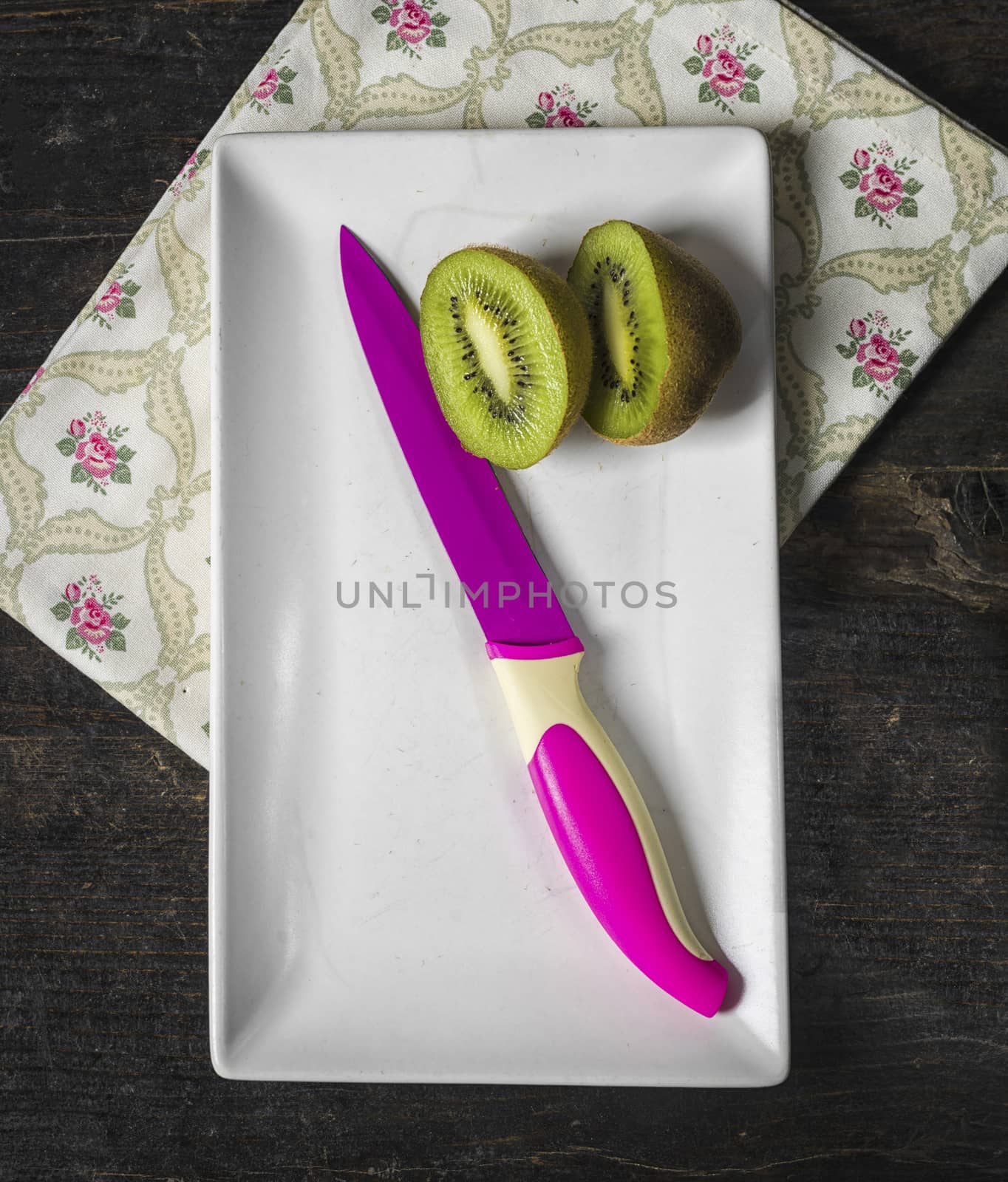 Kiwi fruit and a colored knife over a dark wooden table,