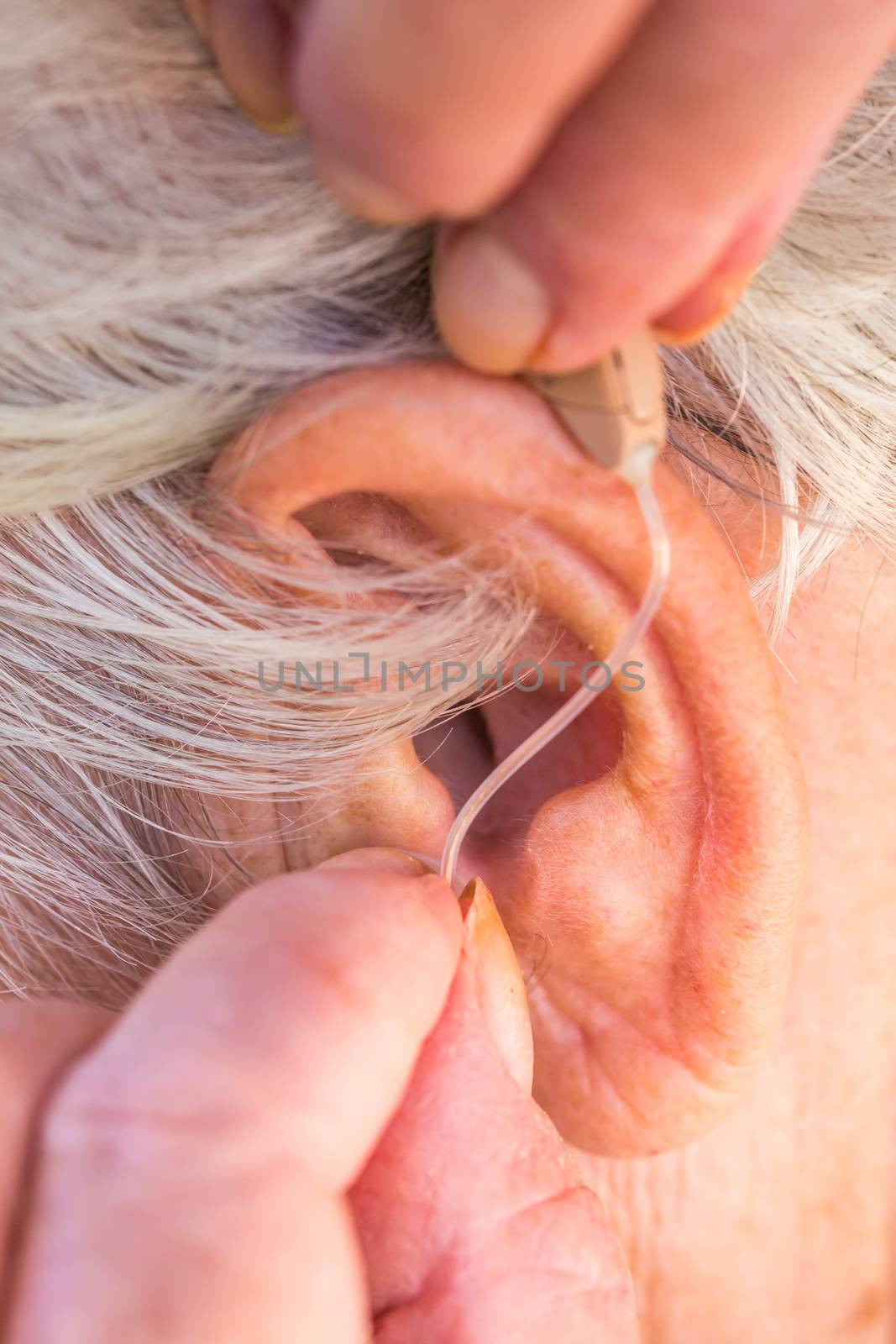 closeup senior woman inserting hearing aid in her ears