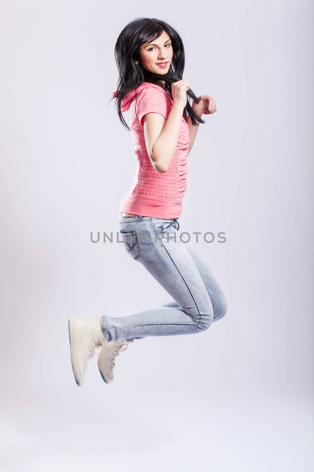 attractive young girl jumping, wearing pink hoodie and jeans