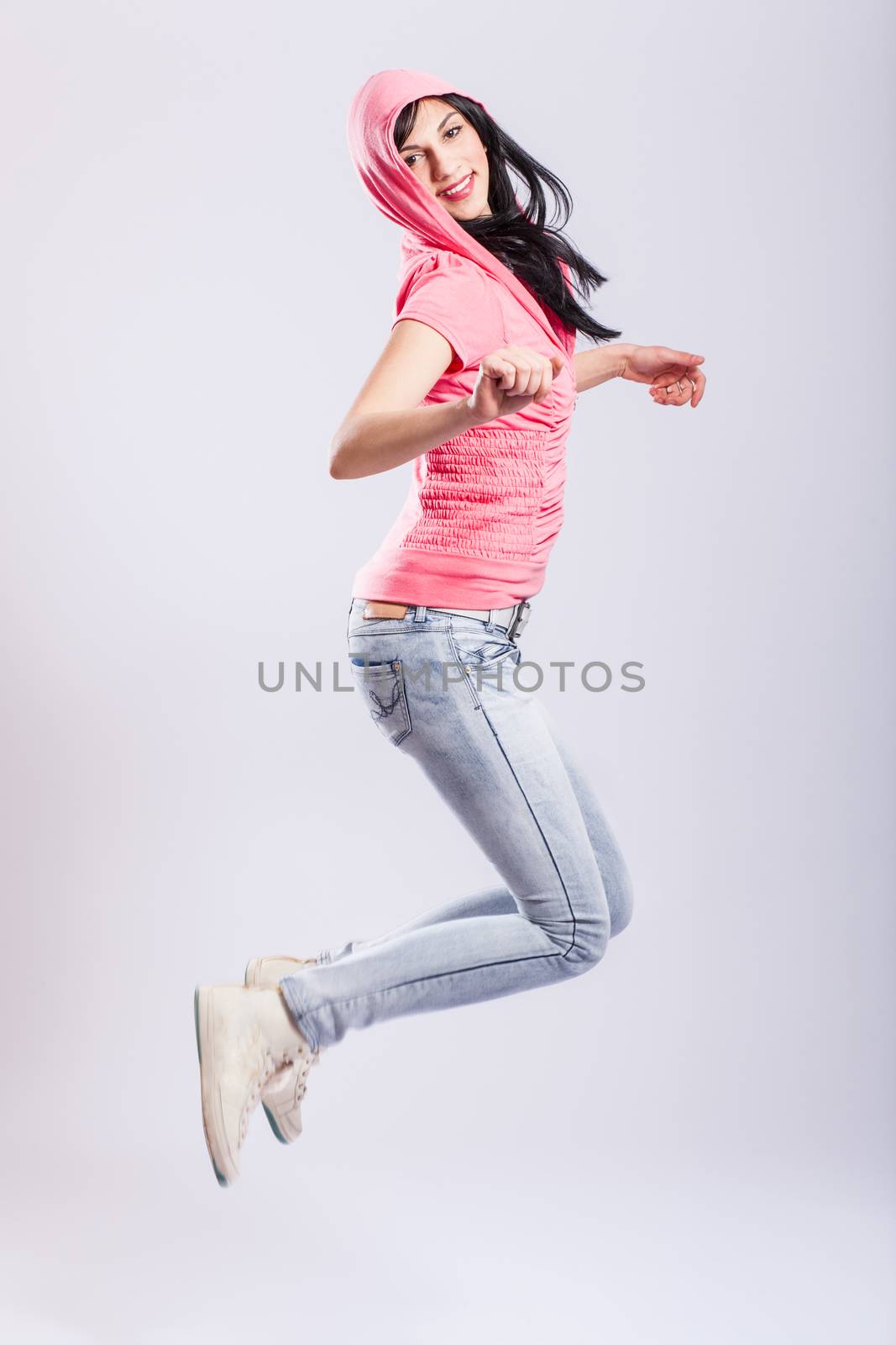 attractive young girl jumping, wearing pink hoodie and jeans